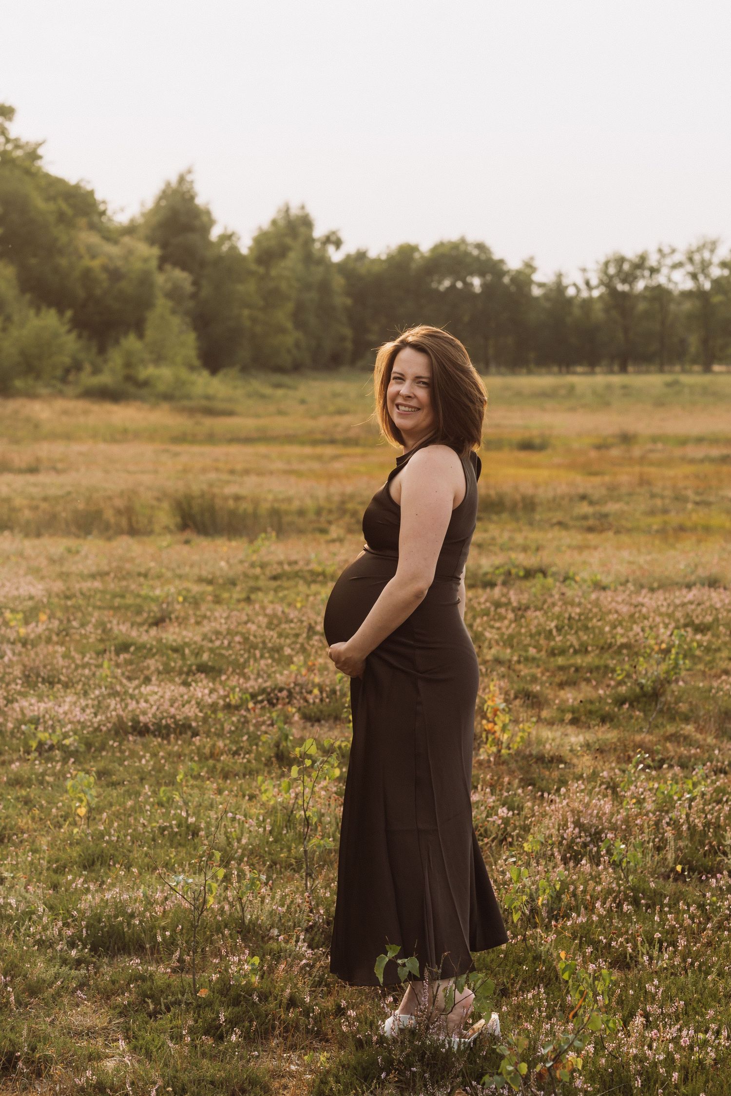 A maternity photoshoot in a wildflower meadow at sunset with warm golden lighting.