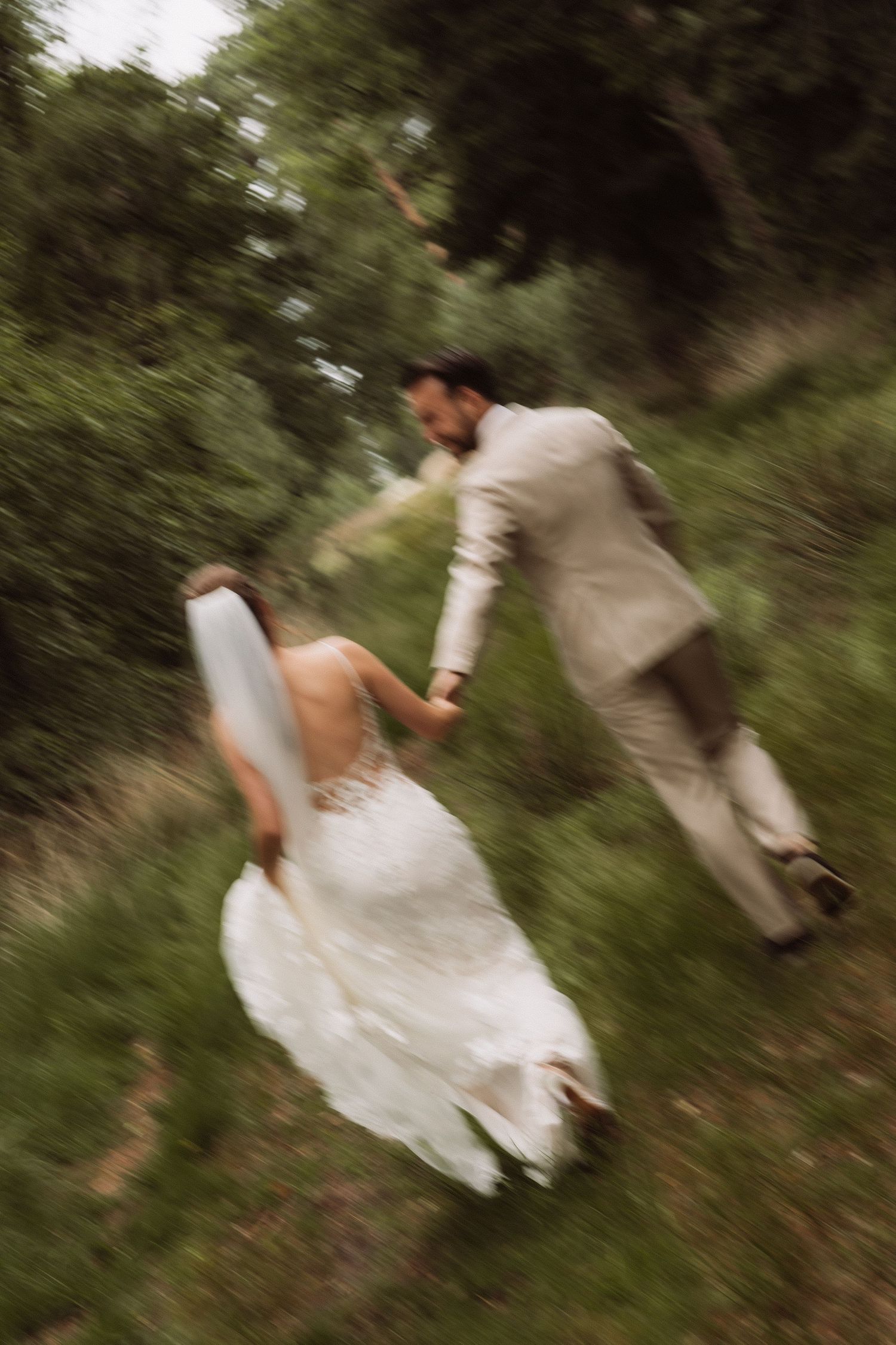 Wedding couple walks through a green meadow with flowing dress and veil creating motion blur.