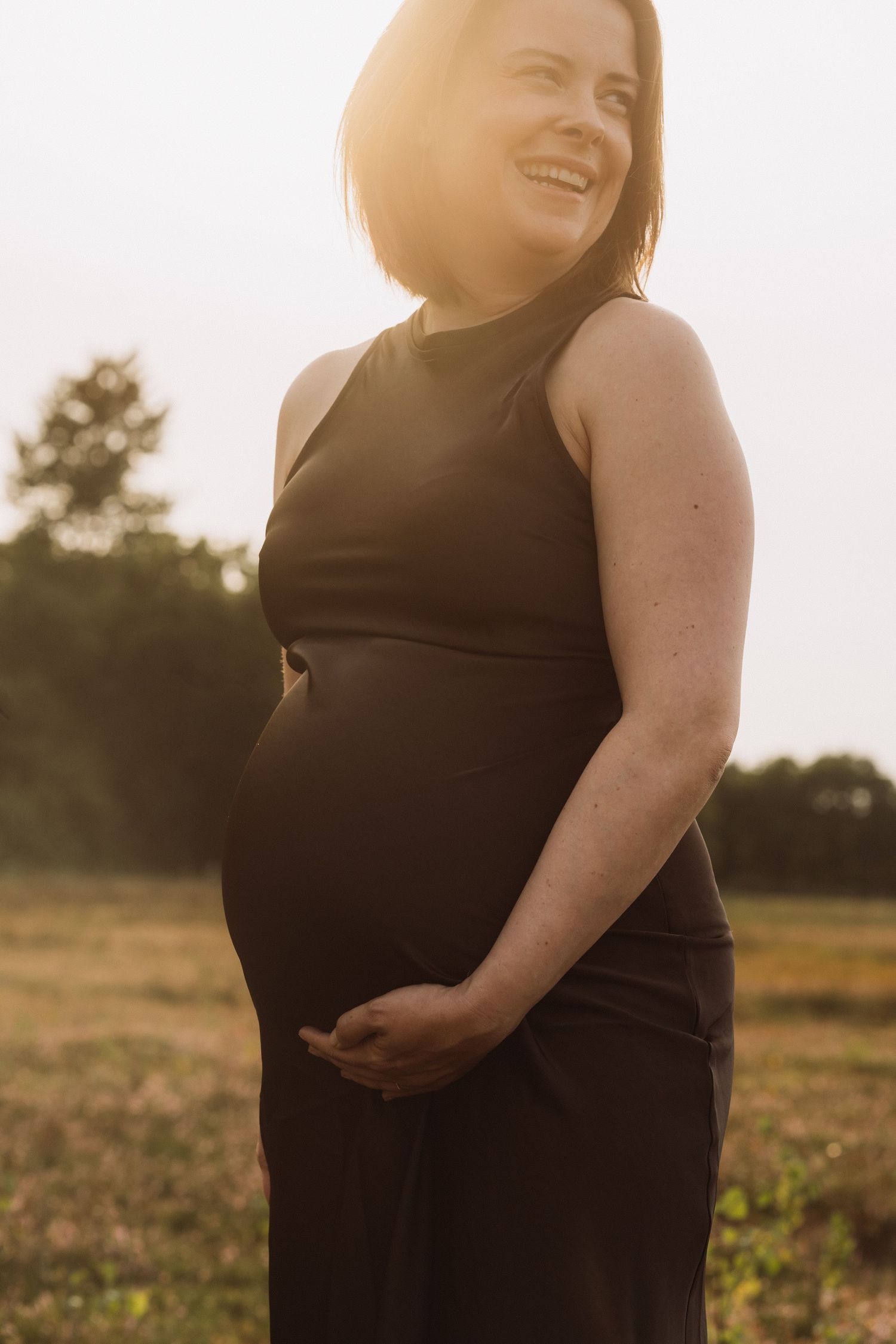 Sunset maternity portrait in black dress showing silhouette against golden sky.