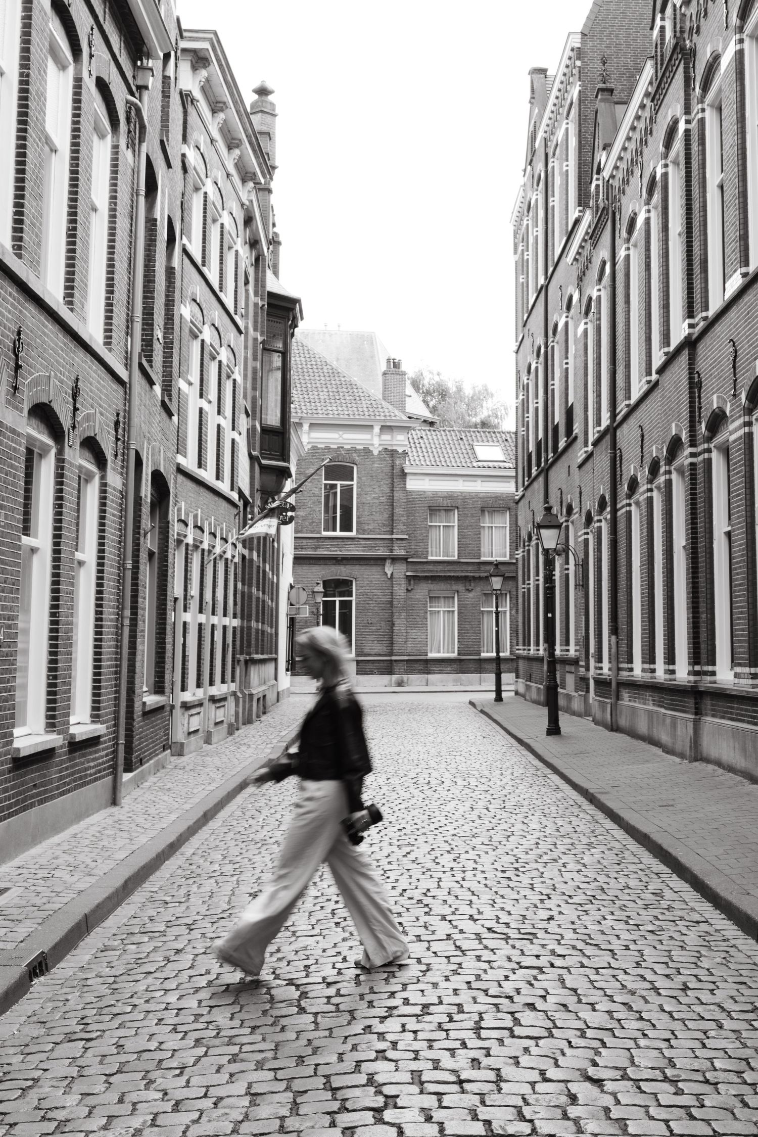 Black and white photo of motion blur on a cobblestone street between historic buildings.