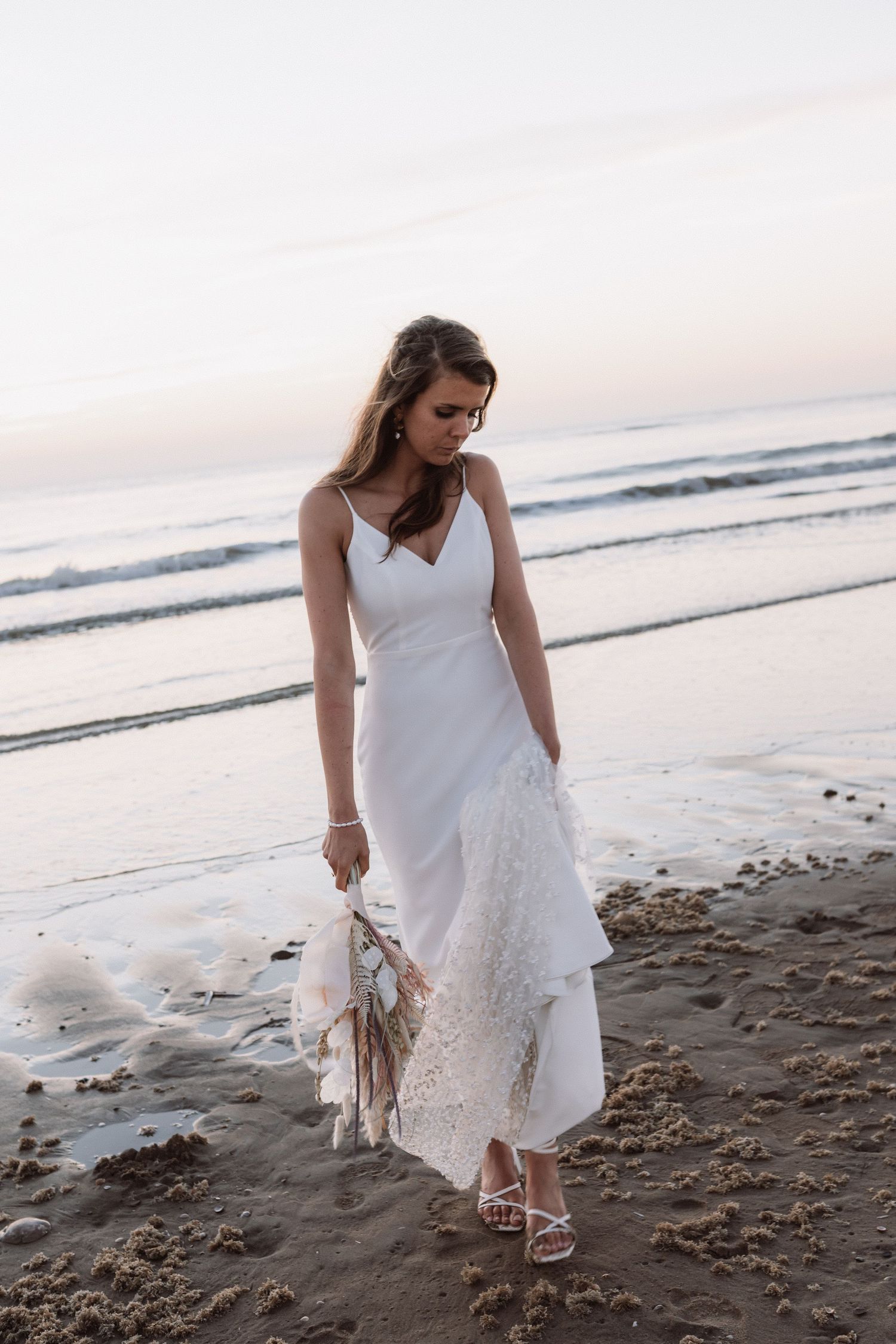 Woman in flowing white dress exploring the sandy beach at dusk.