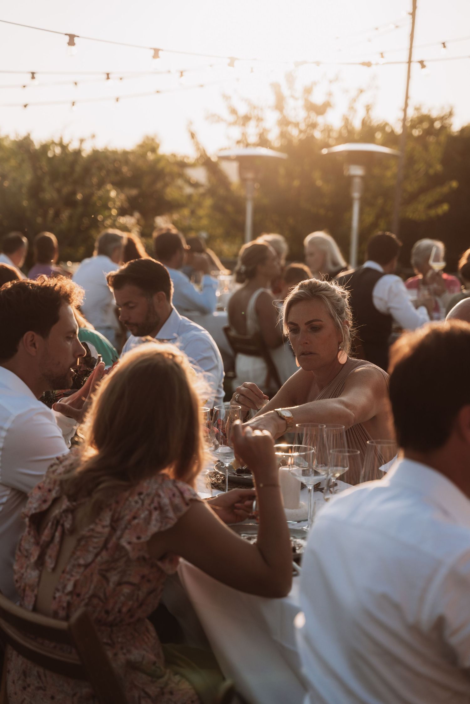 People gathered at an outdoor dinner party during golden hour with string lights overhead.