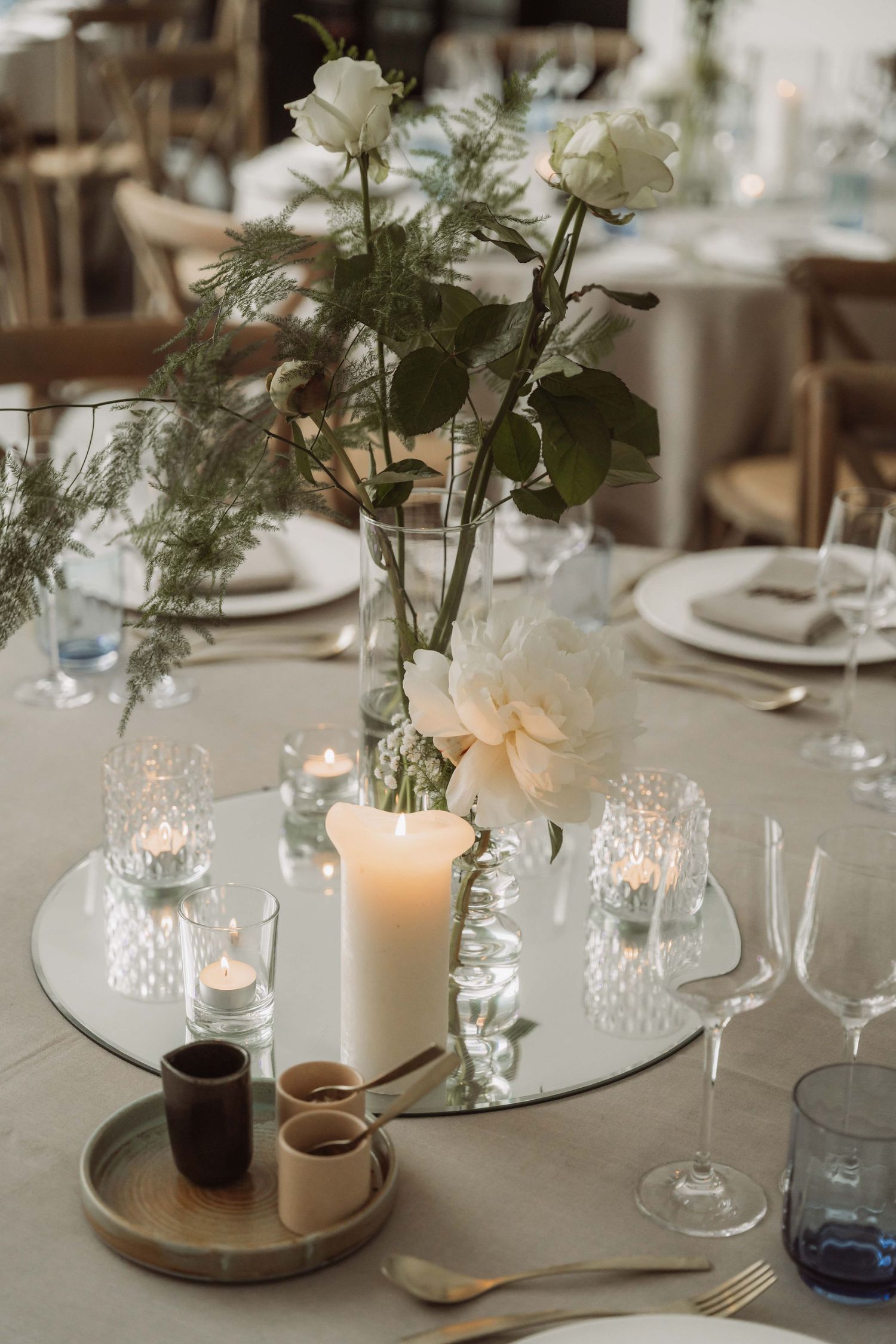 Wedding table centerpieces featuring white floral arrangements, candles, and glass votives on round mirrored trays.