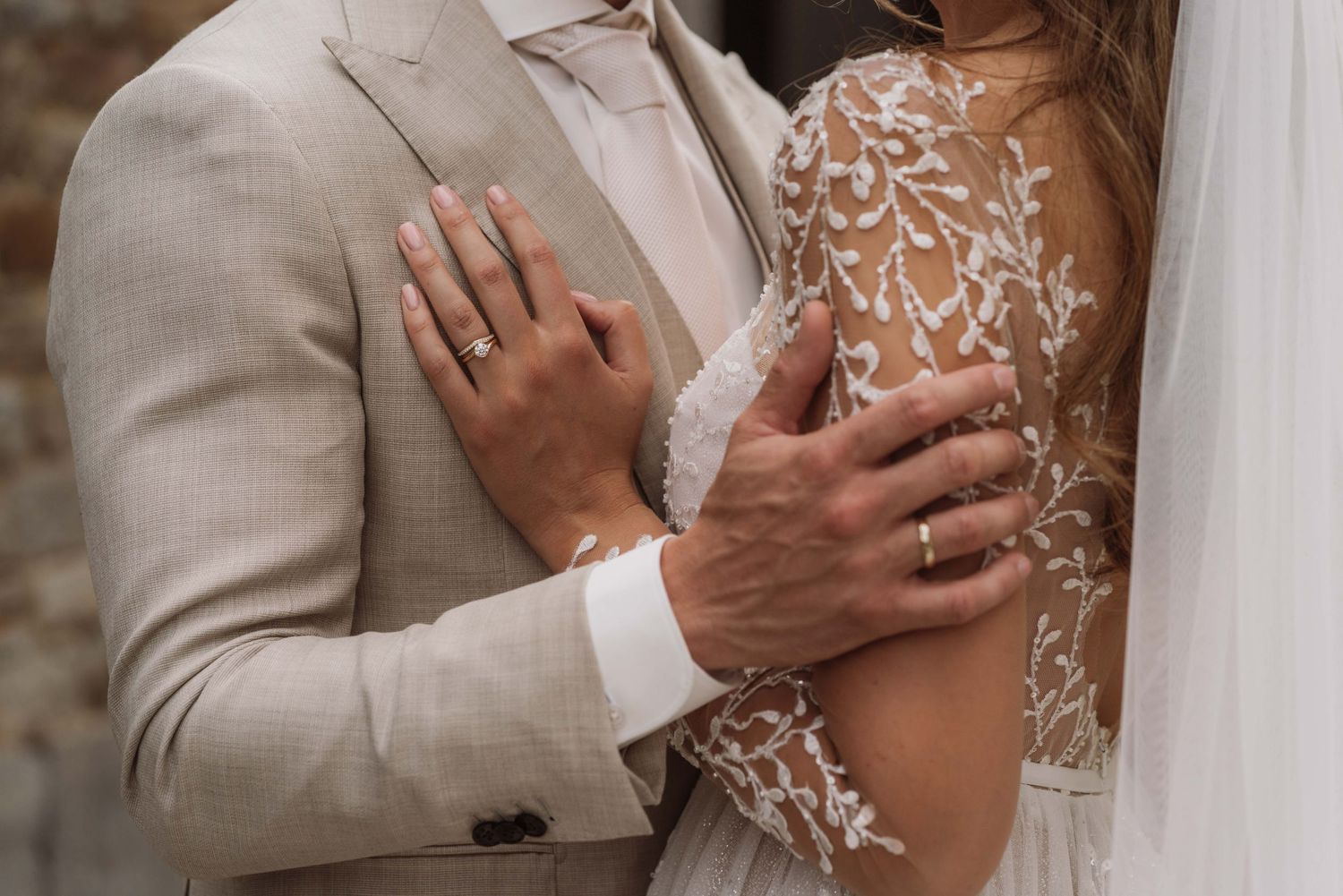 Close-up detail of a couple embracing in wedding attire with delicate lace details and beige suit visible.
