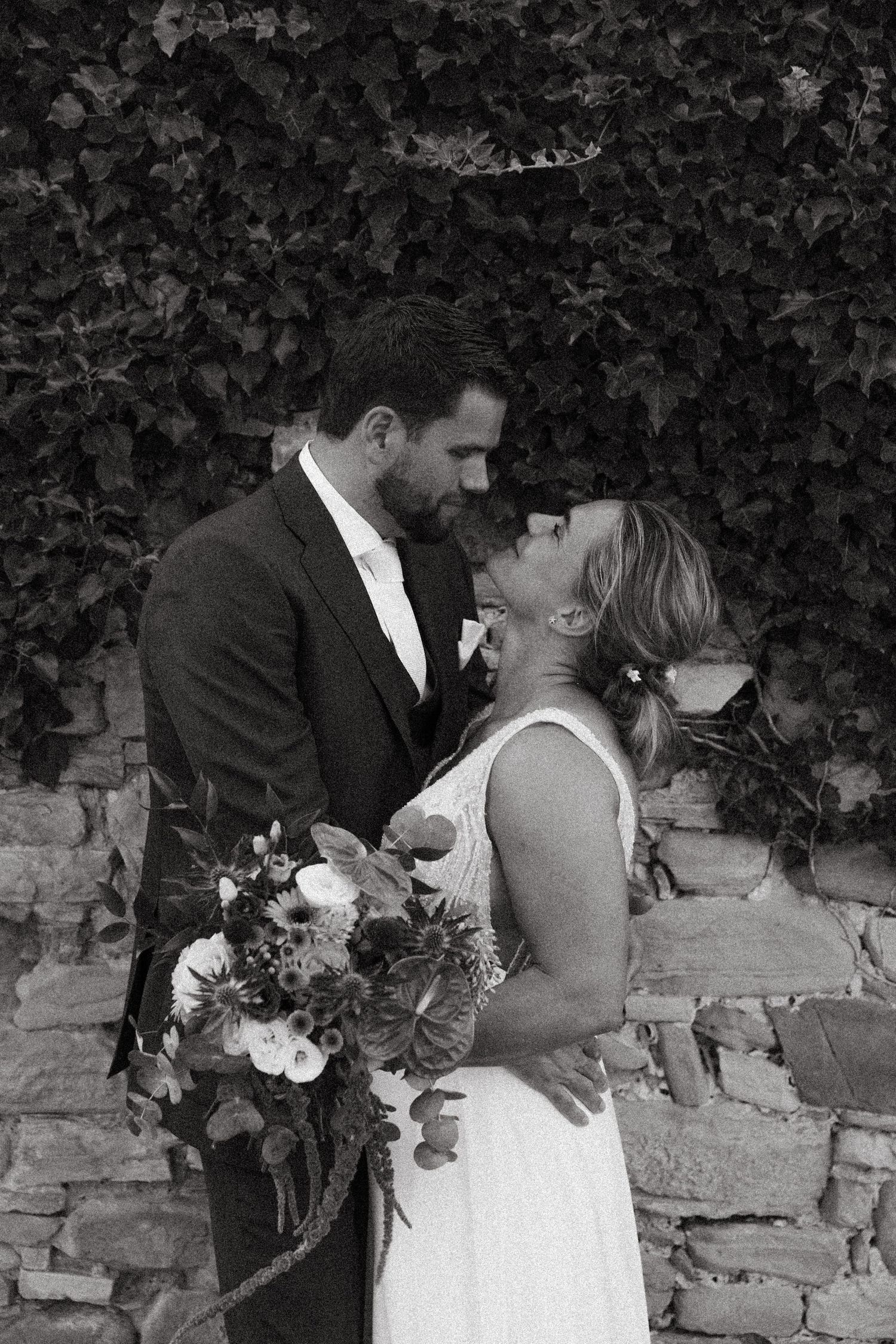 A couple shares a romantic moment against a rustic stone wall backdrop during their wedding photoshoot.