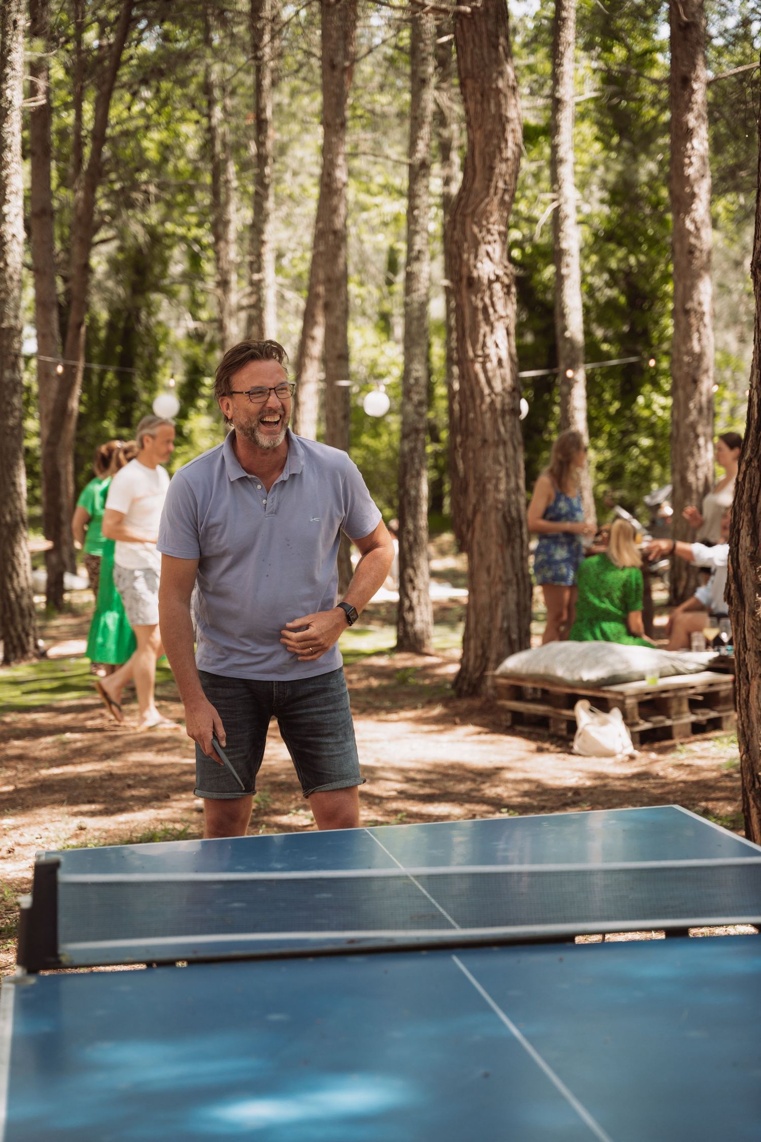 People enjoying outdoor table tennis in a wooded forest area on a sunny summer day.