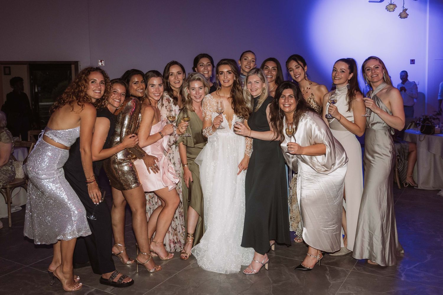 Wedding party group poses together at reception venue with purple ambient lighting in the background.