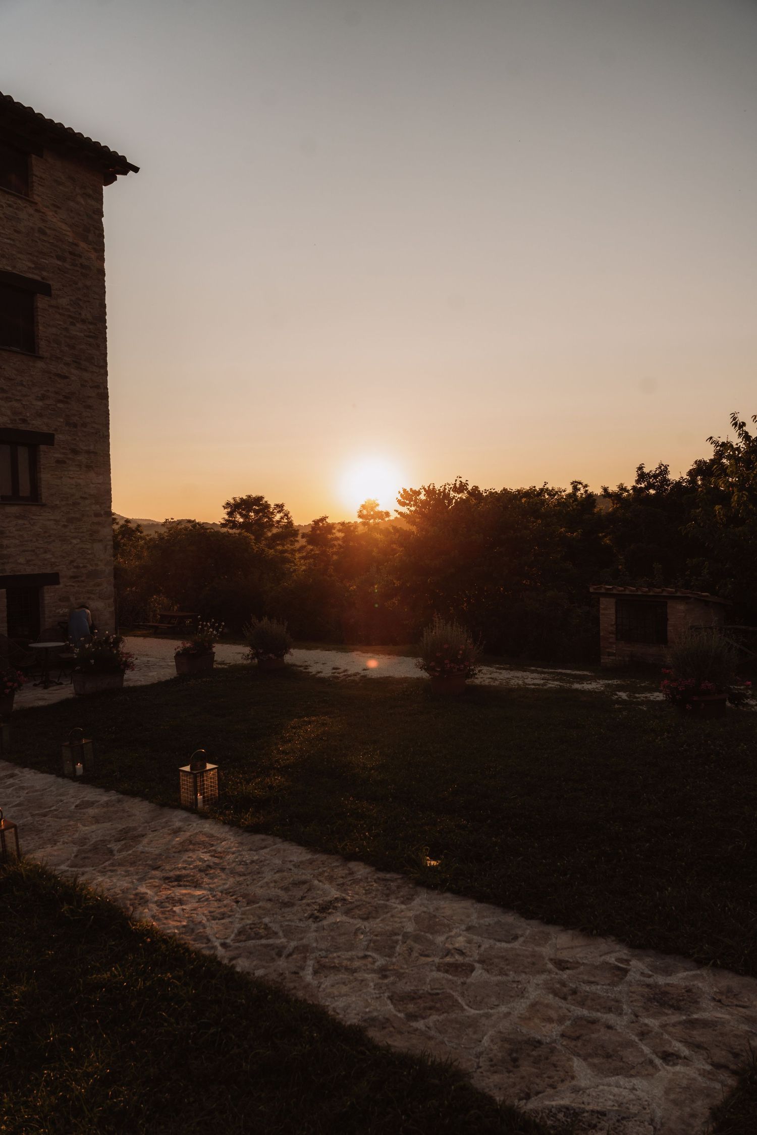 Scenic sunset view over a rustic stone wall with golden sunlight filtering through trees in the distance.