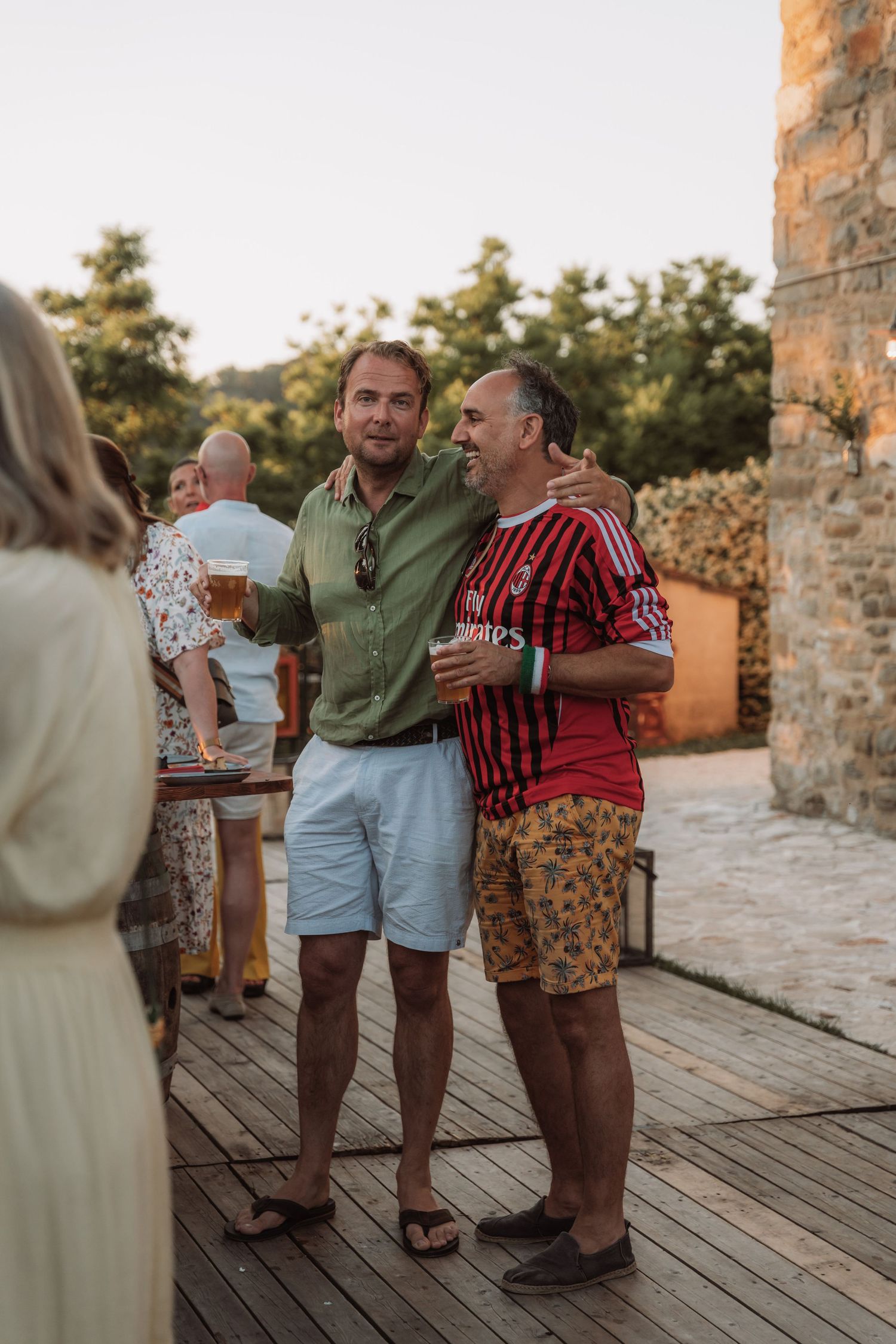 People enjoying drinks and conversation at an outdoor gathering on a wooden deck during golden hour.