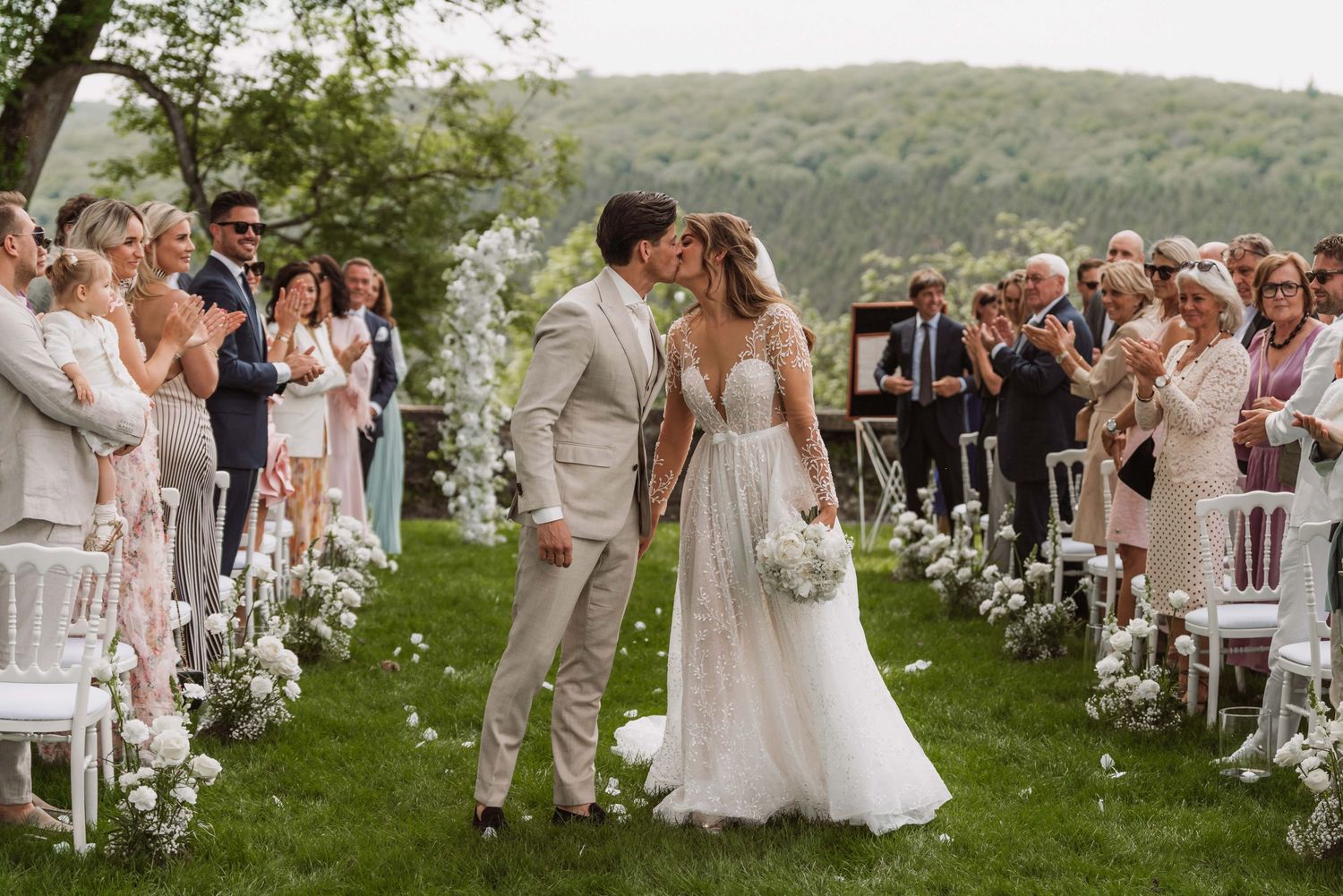 Outdoor wedding ceremony setup with white chairs and floral arrangements on a lush green lawn.