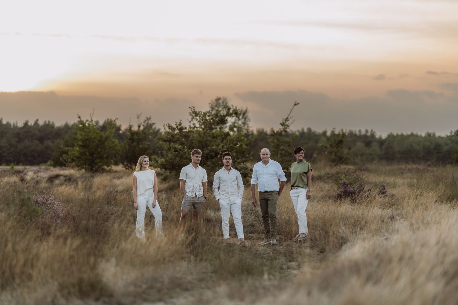 Family group photo silhouetted against sunset in golden field wearing white outfits.