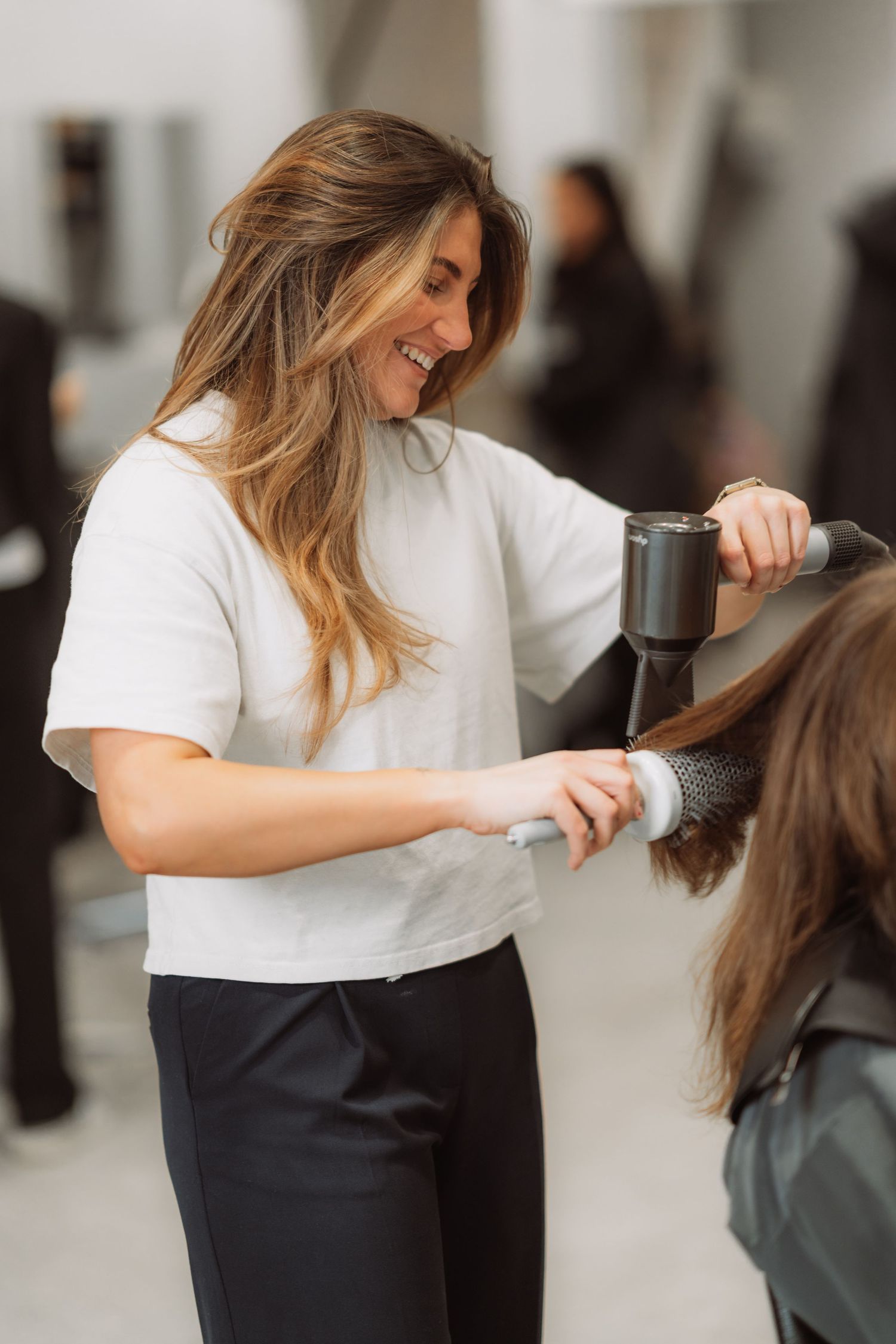 Stylist using hairdryer and round brush for professional blowout.