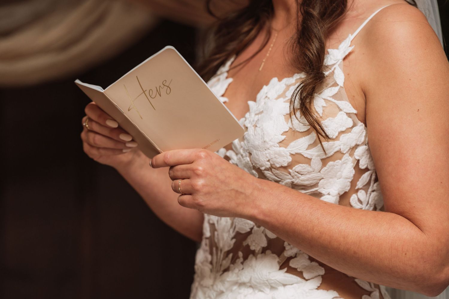 A person in a white wedding dress holds and reads from a small book during a ceremony.