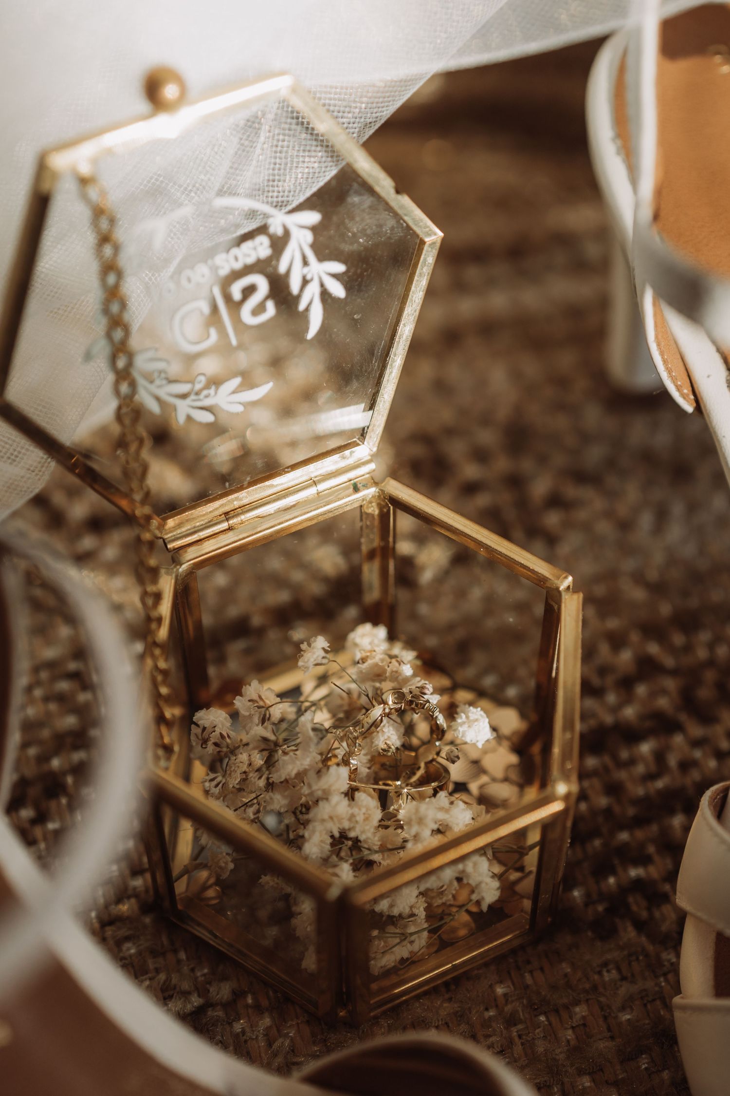 Small dried flowers and petals displayed in a delicate hexagonal glass and gold jewelry box.