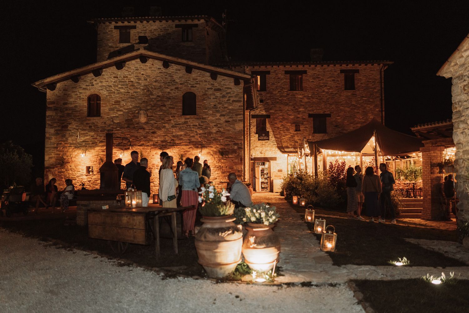 Historic stone buildings illuminated at night create a rustic ambiance during an outdoor evening event.