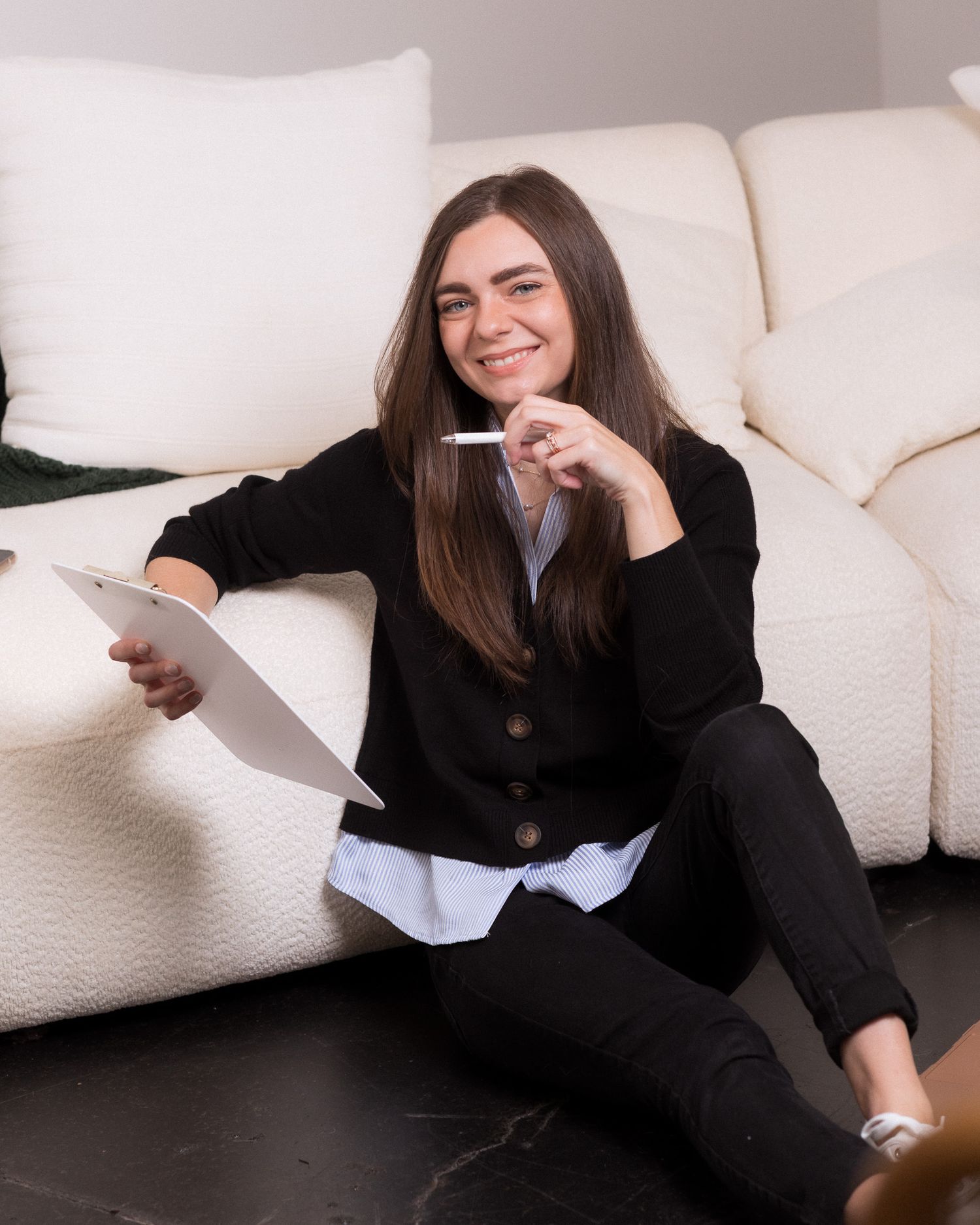Smiling young woman sitting for personal branding, holding a notepad, wearing a sweater over a casual shirt. Photo taken in Eugene, OR