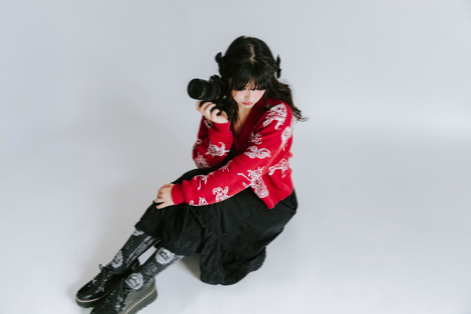Winnie, photographer of Fledermaus Visual, sitting on a white background with a camera in her hand.