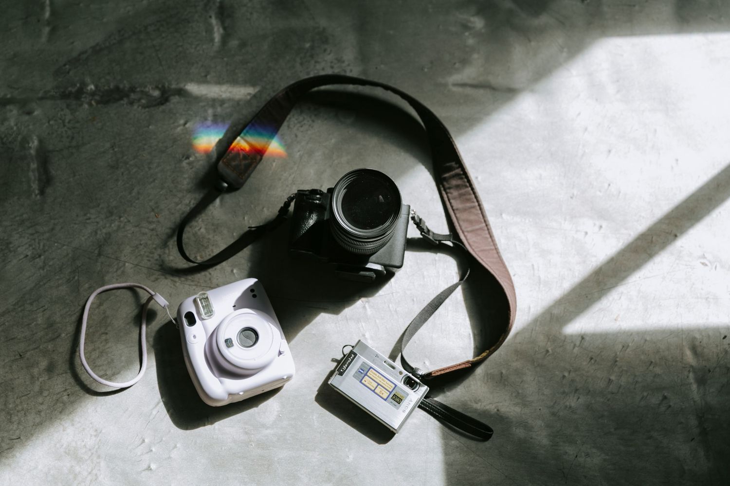 A flatlay photo of various cameras struck by a beautiful window light and a rainbow, part of a branding suite.