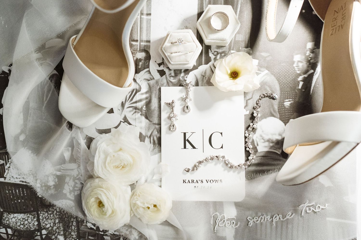 Wedding accessories including white shoes and roses arranged with monogram card.