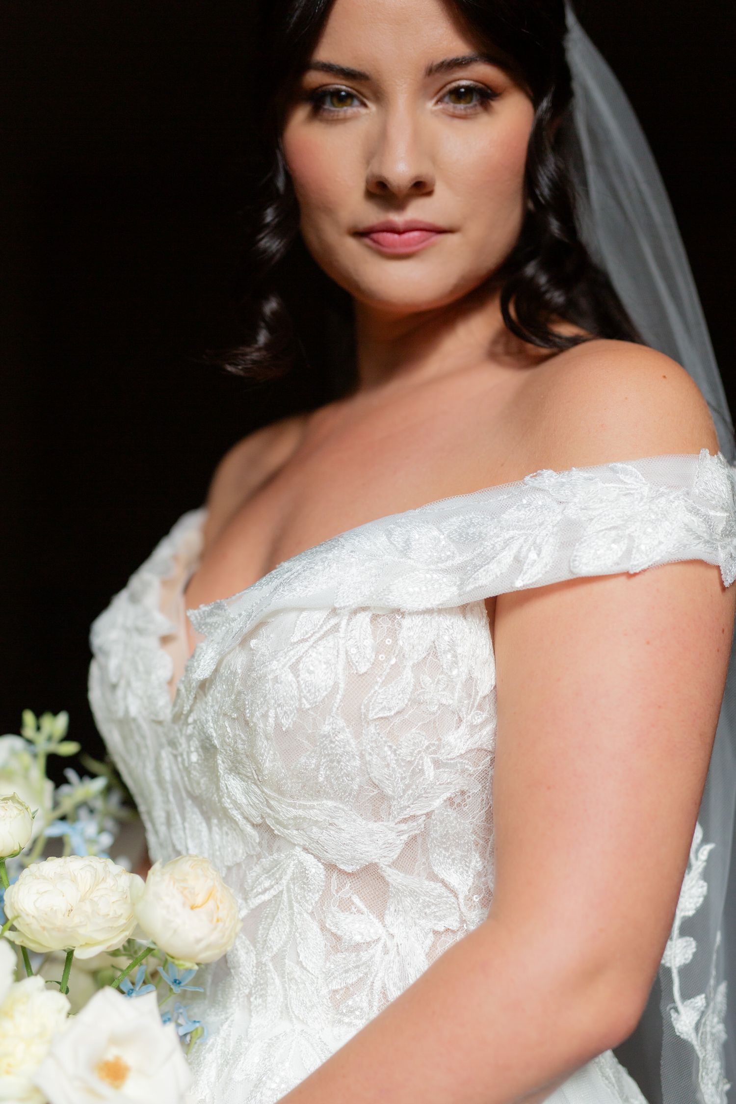 Close-up of an off-shoulder white lace wedding dress with delicate embroidery details.