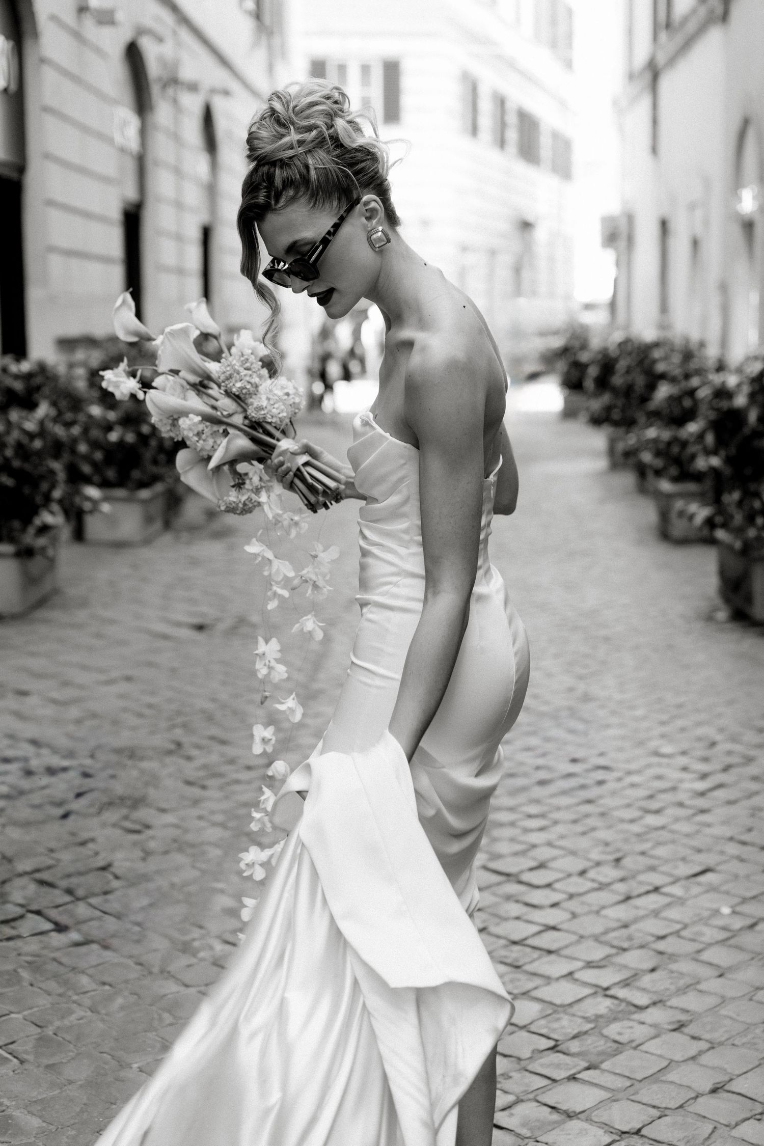Elegant bridal portrait on cobblestone street carrying white floral bouquet.