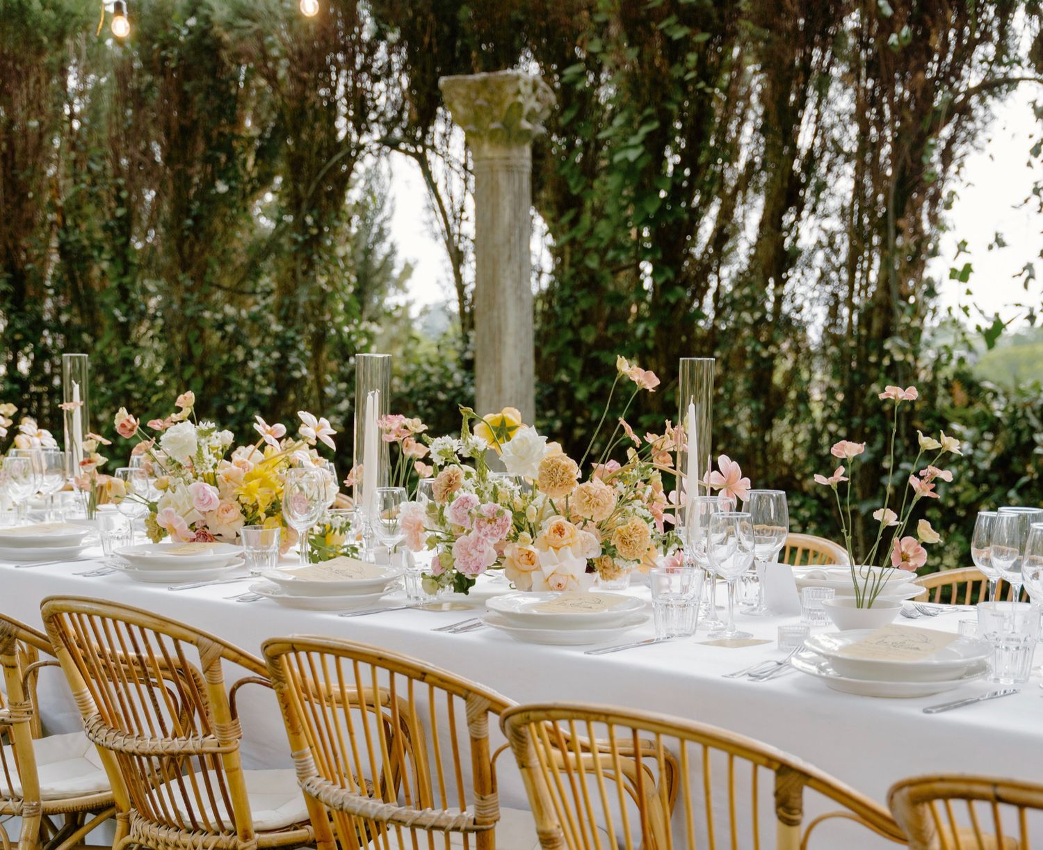 Outdoor wedding reception setup with wooden chairs and white table settings under natural canopy.