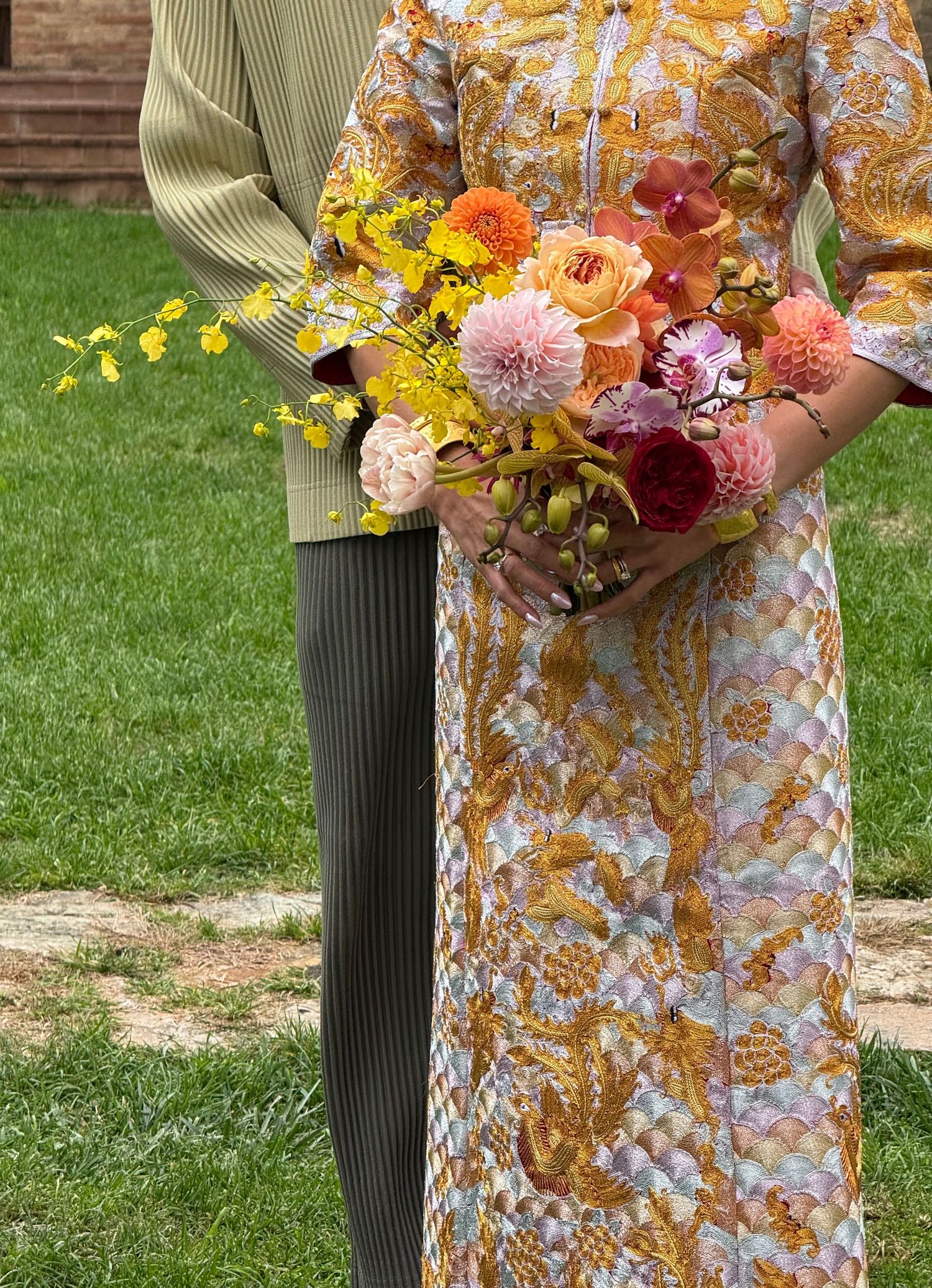 Person wearing yellow and floral dress holding vibrant autumn-colored flower bouquet.