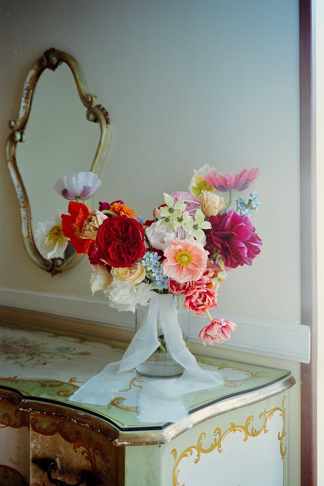 Colorful flower arrangement in white vases atop an antique painted table.
