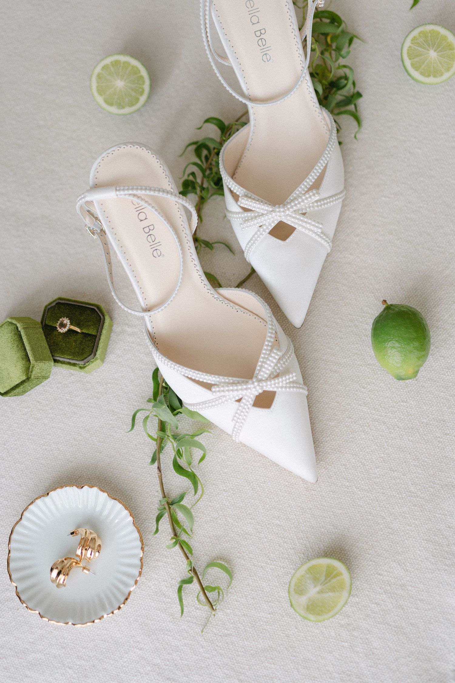 Elegant white bridal shoes displayed with lime slices and seashell accessories on light background.