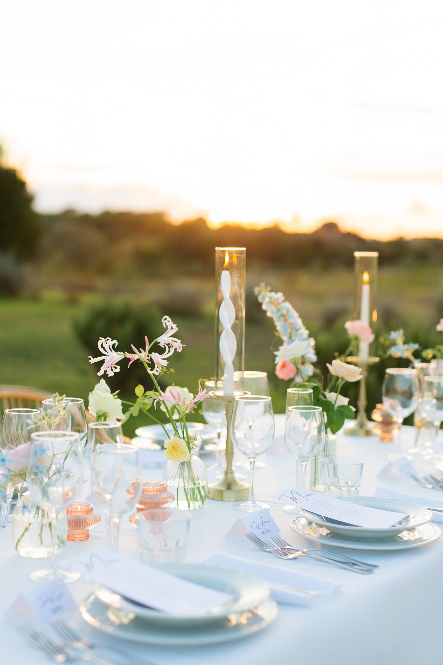 Romantic table setting with delicate floral centerpieces and glassware at sunset.