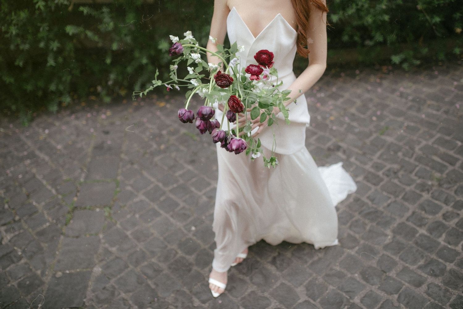 Romantic wedding dress details with delicate lace and flowing fabric against stone pathway.
