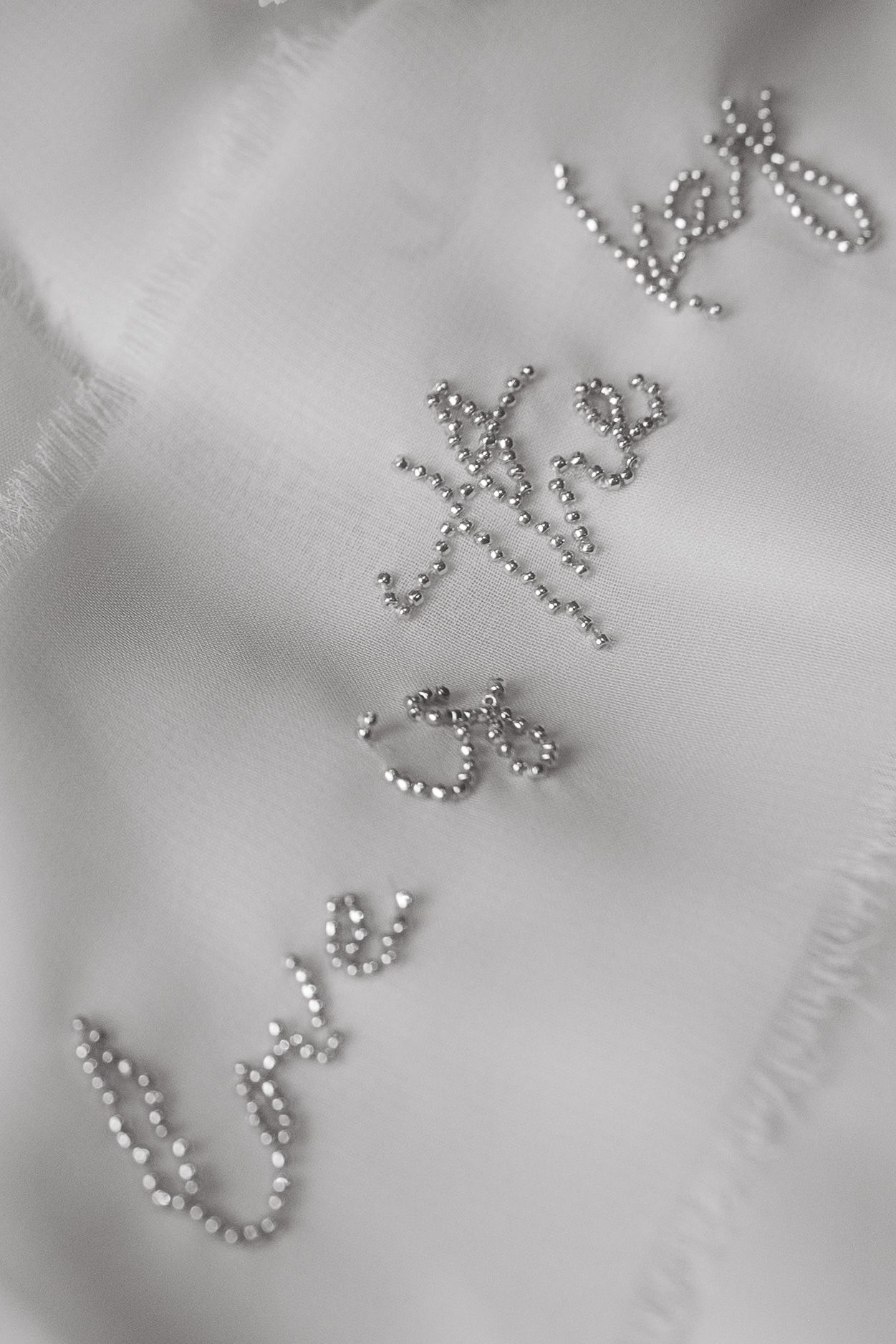 Close-up of cursive text embroidered in silver beading on white fabric.
