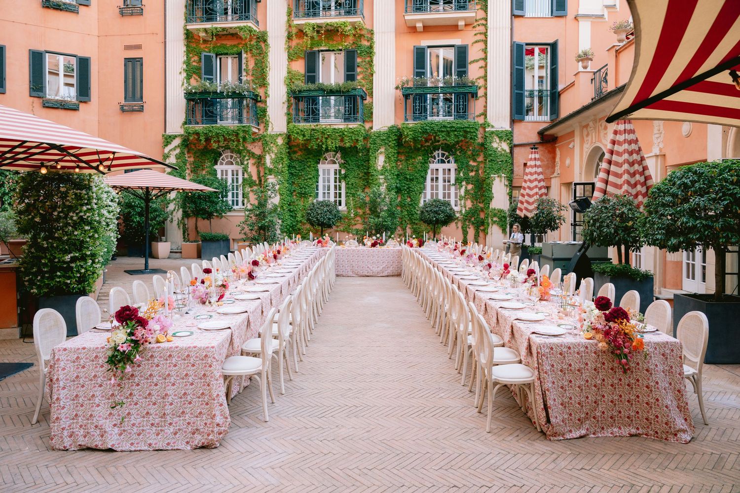 Outdoor wedding reception setup in Mediterranean courtyard with pink floral tablecloths and white chairs.