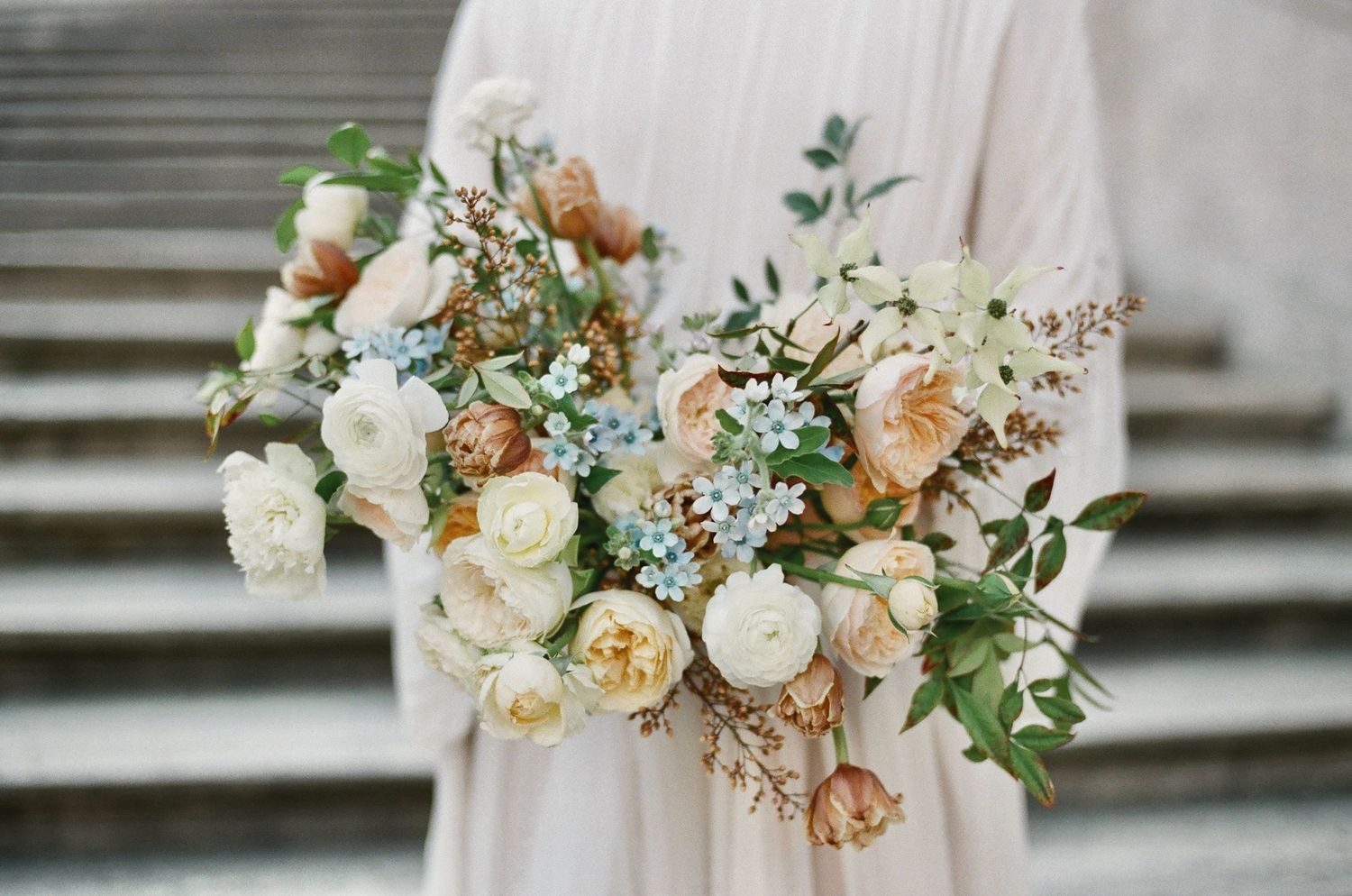 Delicate peach and cream wedding bouquet with roses and mixed flowers against neutral background.