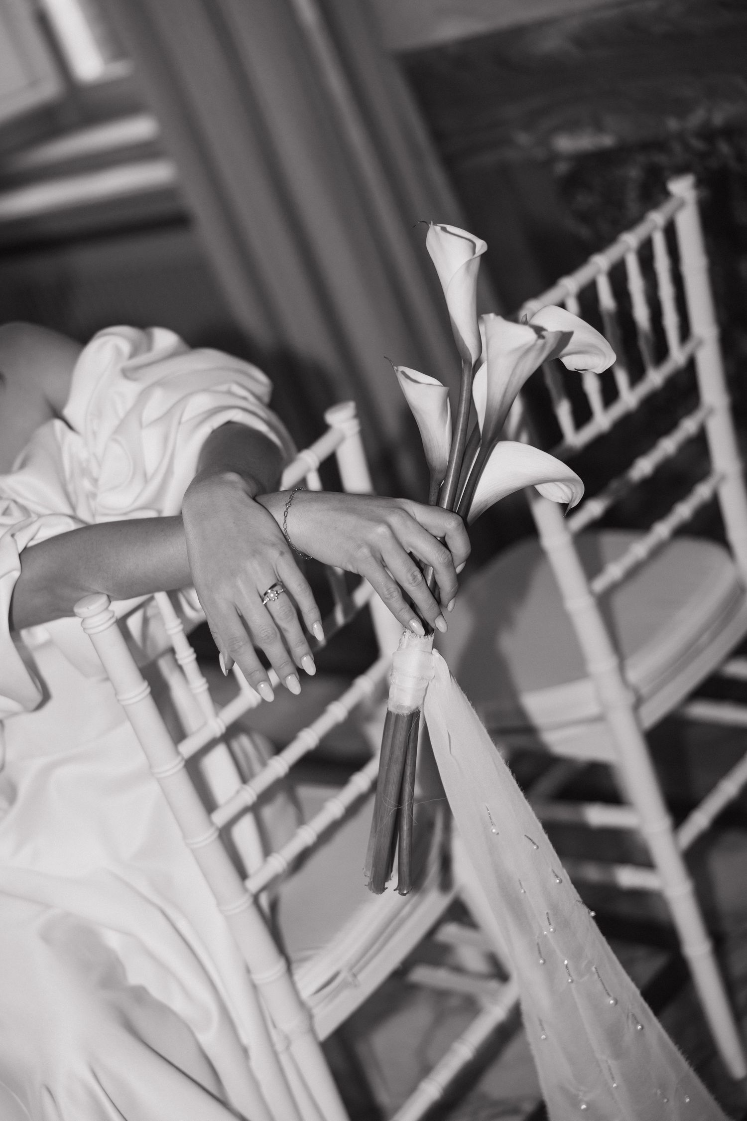 Black and white detail shot of hands holding calla lilies against white fabric.