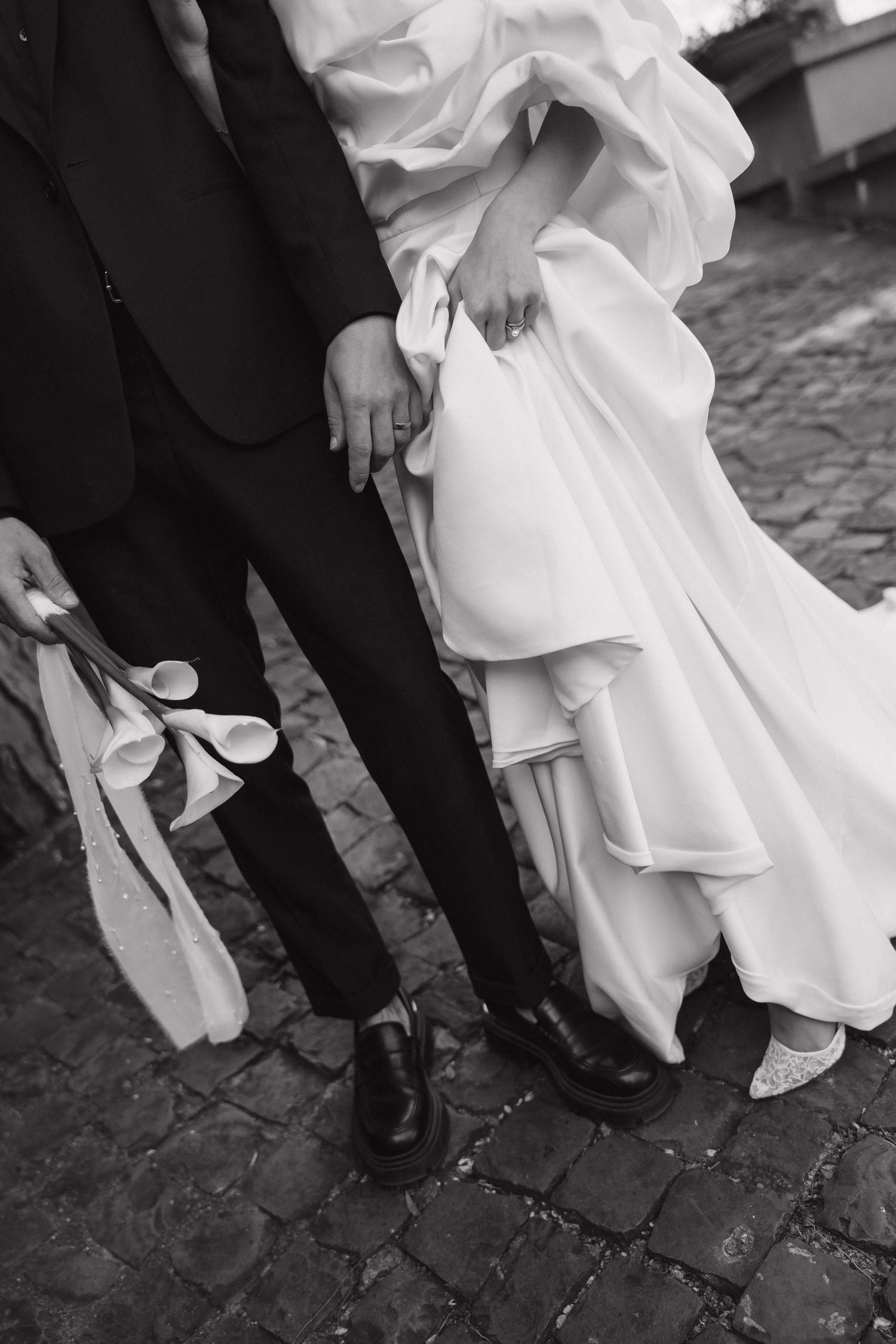 Black and white photo showing wedding dress hem and formal shoes on cobblestone.
