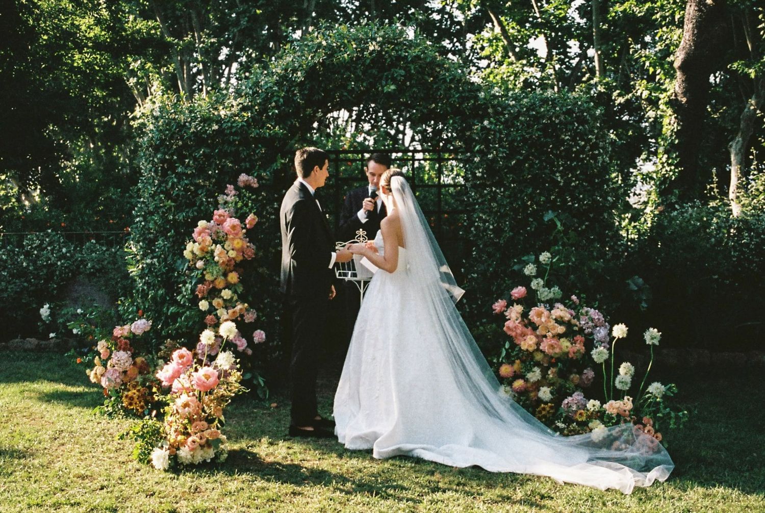 Wedding couple embraces in garden setting with peach floral arch installation.