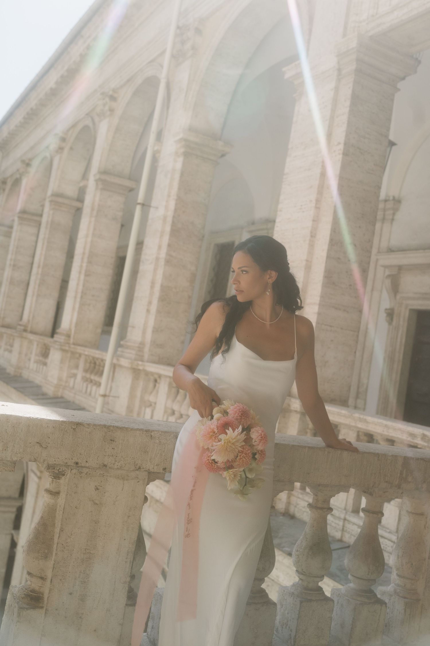 Elegant white wedding dress photographed against classical stone architecture.