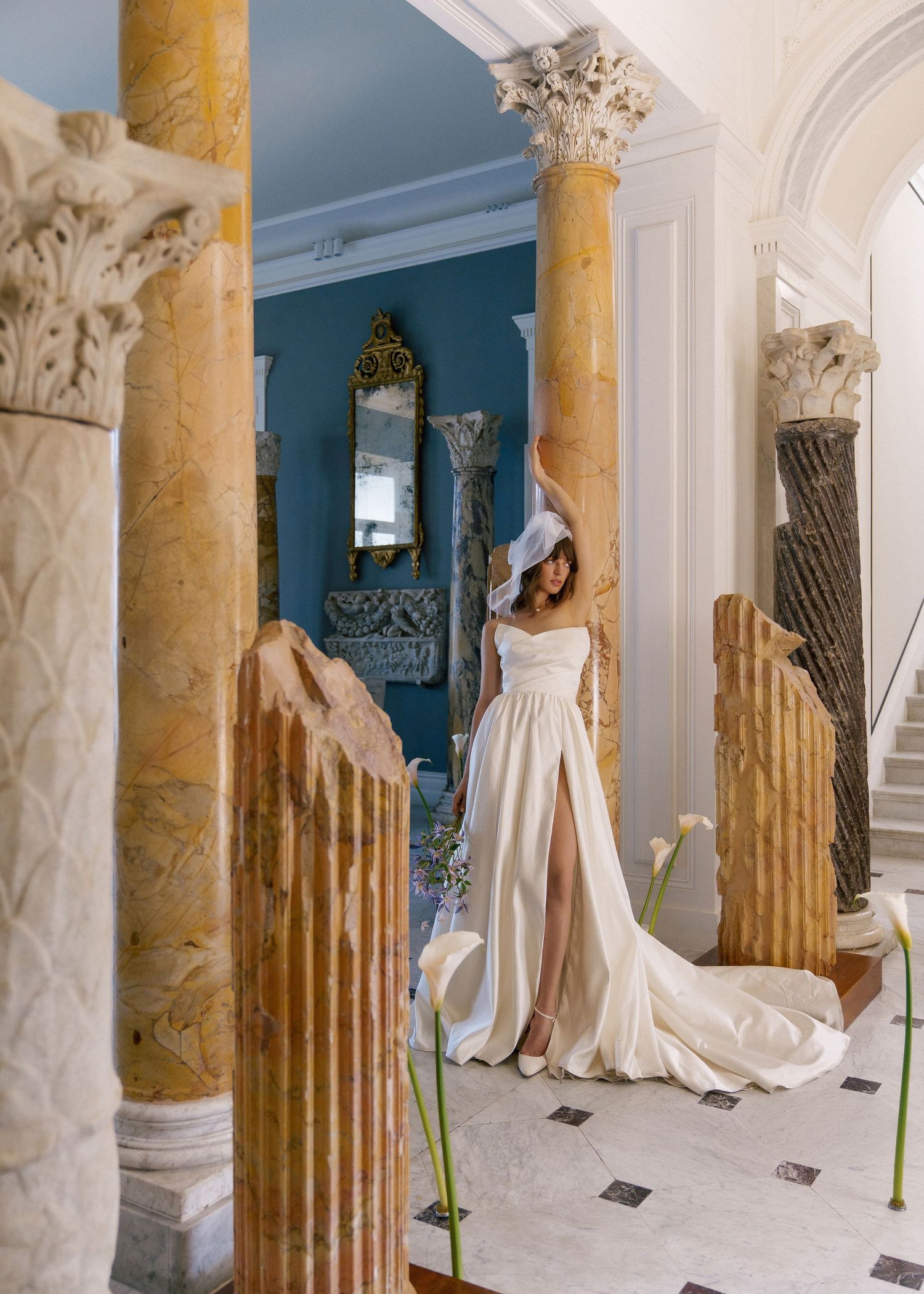 Wedding dress display in grand interior with golden columns and ornate architectural details.