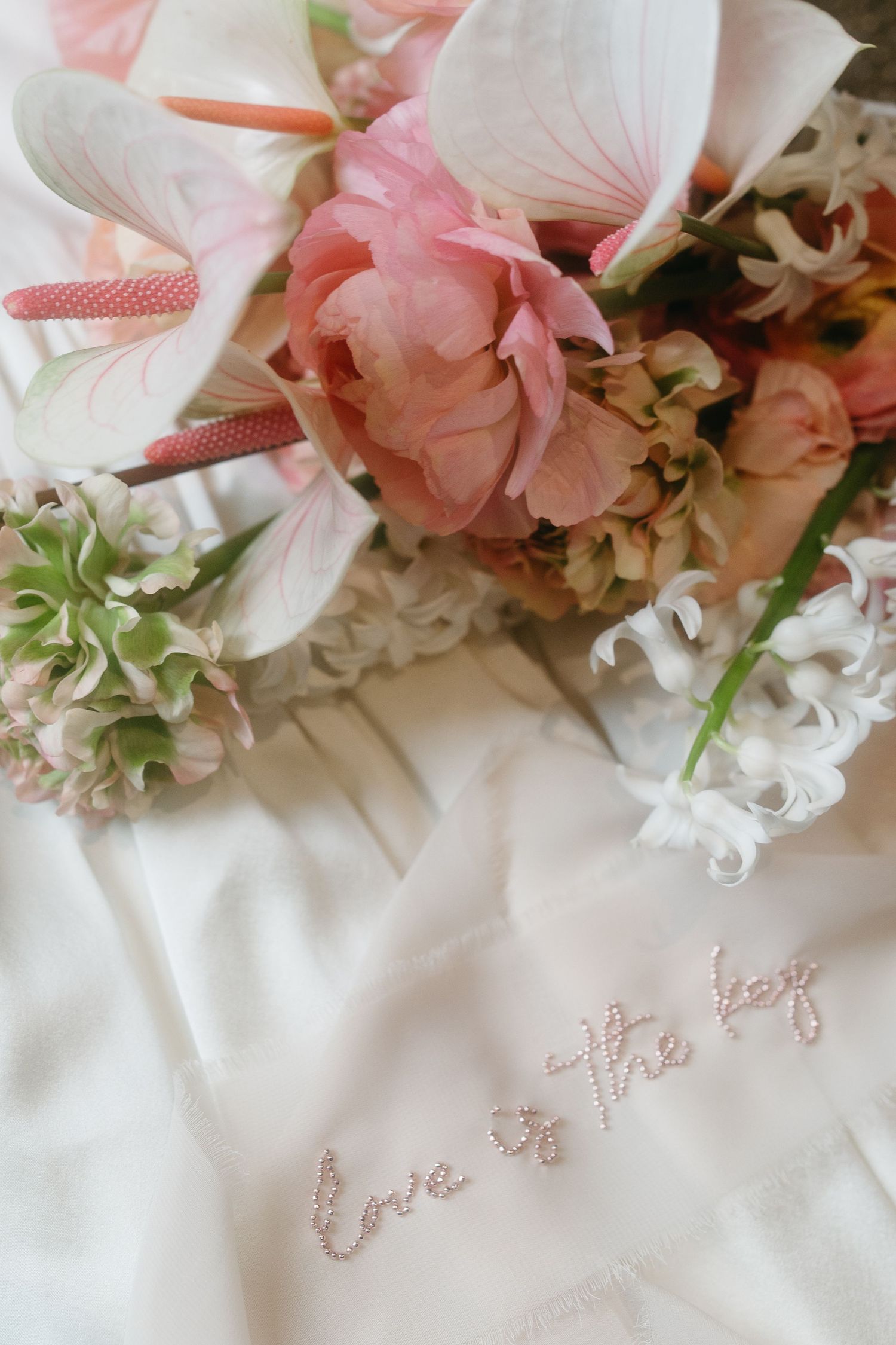 Pink floral arrangement with embroidered 'Love' text on white fabric.