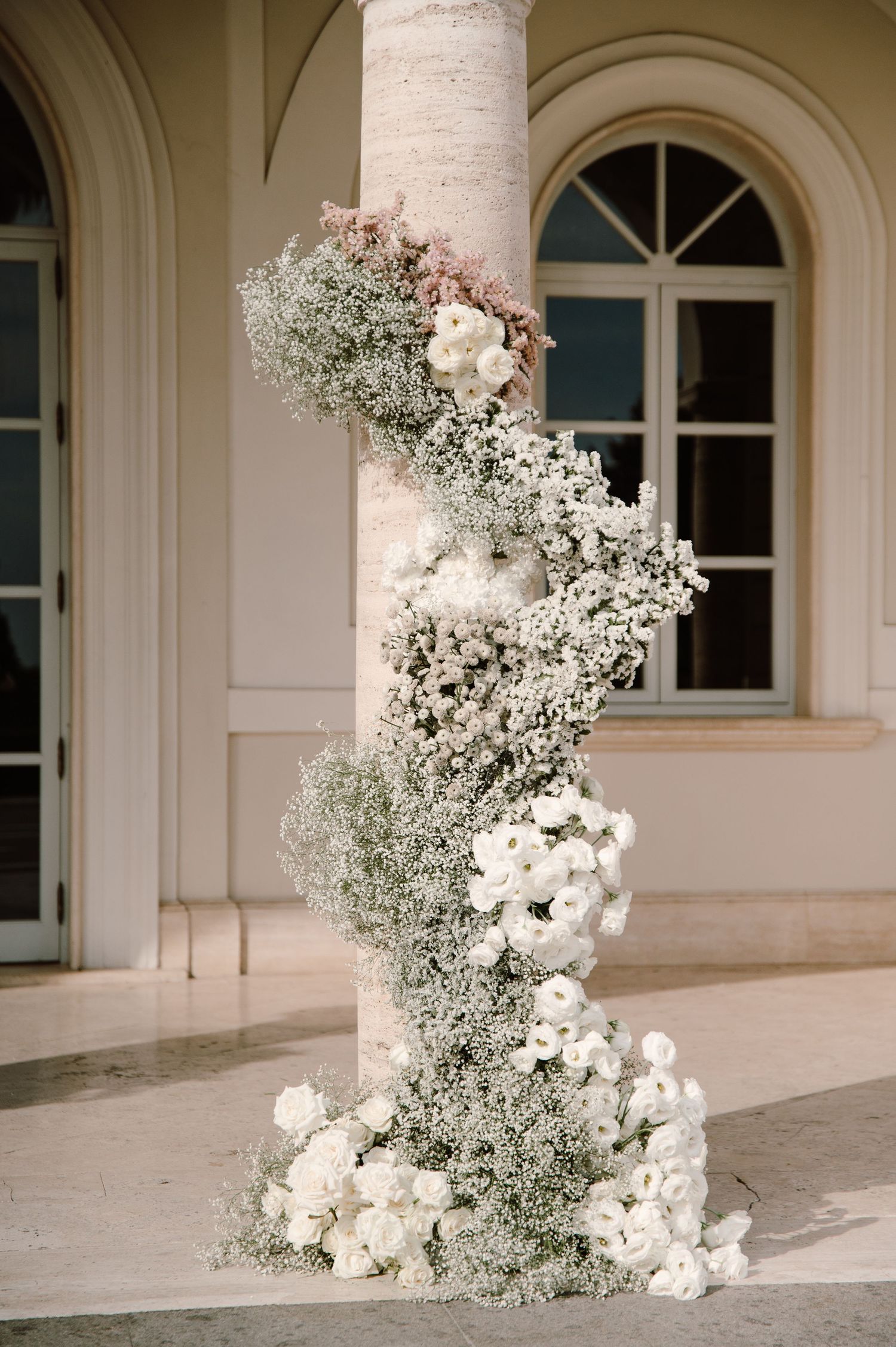 White floral arrangements with baby's breath decorate elegant cream-colored stone columns.