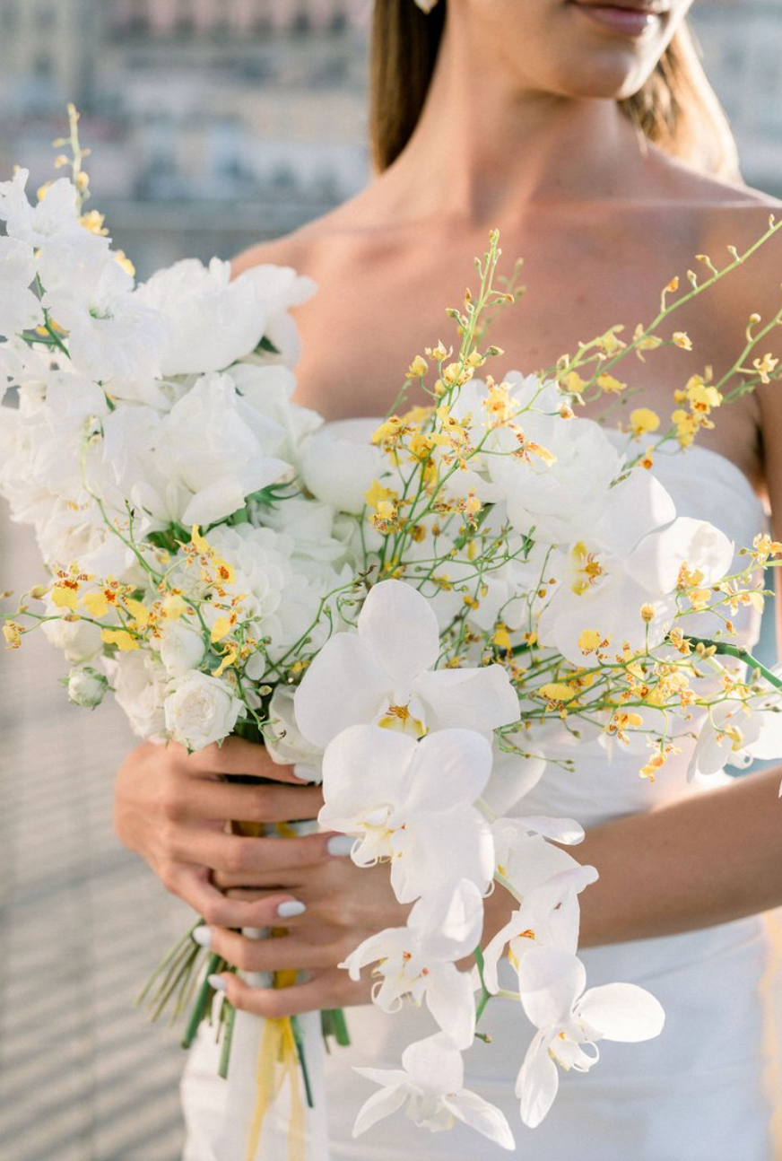 Elegant white orchid and yellow flower bouquet held against a light background.