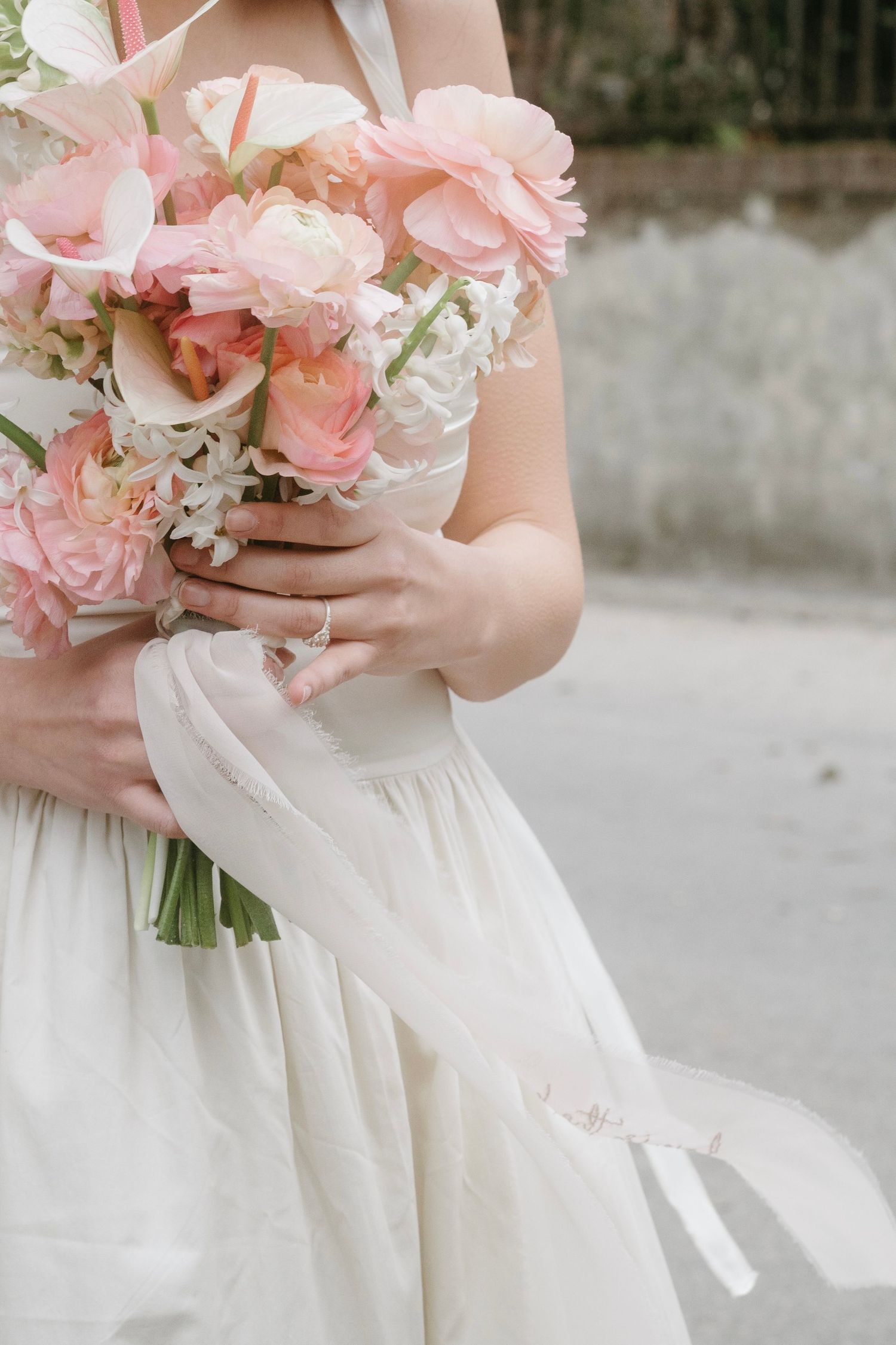 Delicate pink and white bridal bouquet held against a white wedding dress.