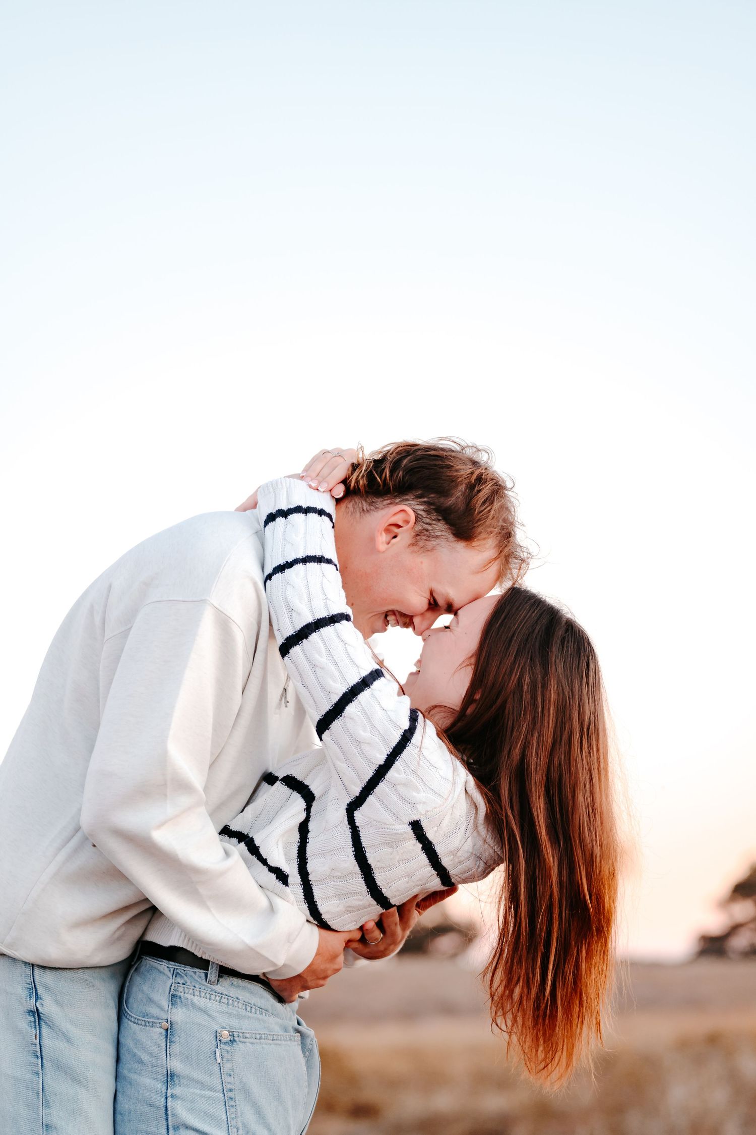 A COUPLE LOVINGLY TOUCHING NOSES AND GRINNING AT ONE ANOTHER, A NATRUAL MOMENT OF BEAUTIFUL CONNECTION