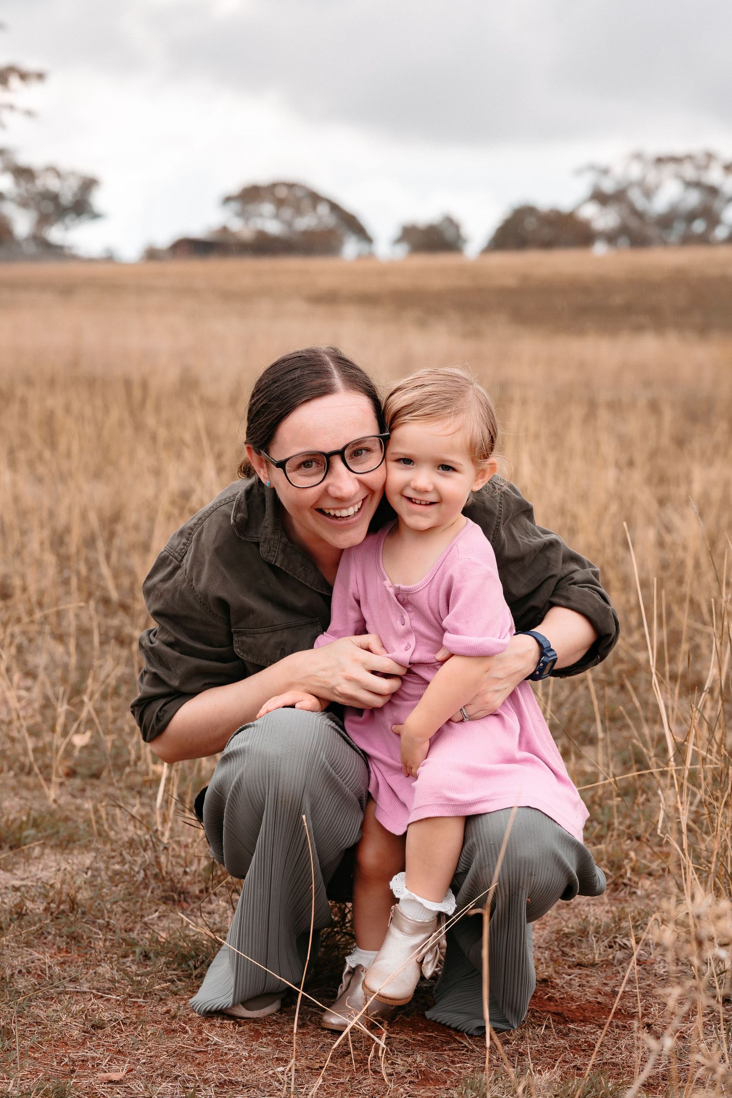 happy down to earth mum cuddling cute toddler in a natural open paddock on an overcast day