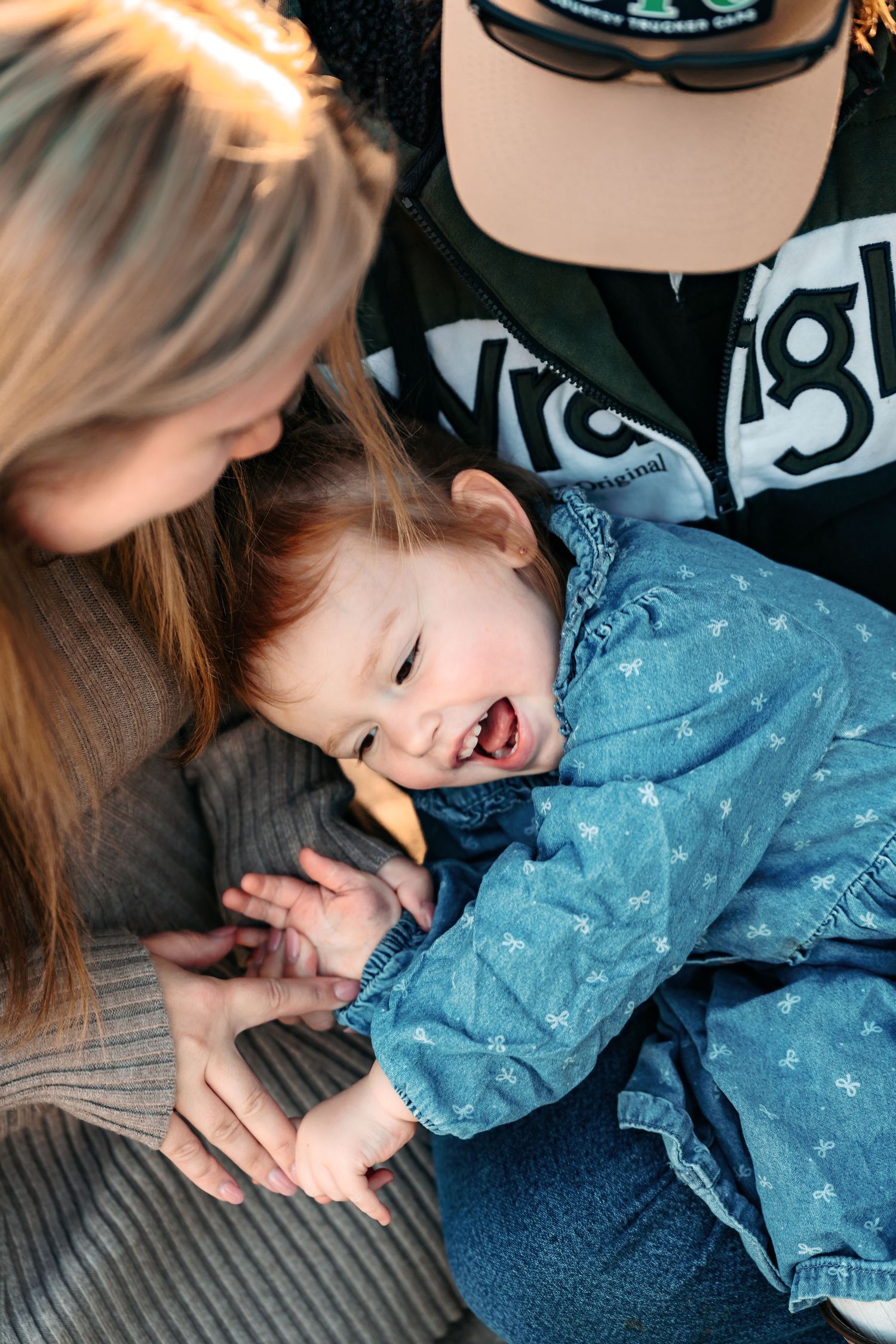 a mum and dad tickling their little 3 year old daughter who has a cheeky smile. a relaxed and natural family moment captured