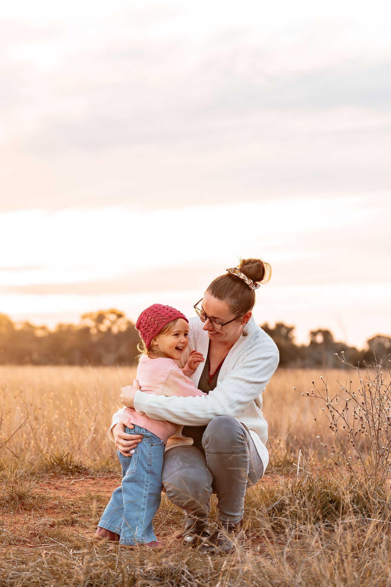 a mum and daughter cuddling and laughing together in a golden field at sunset