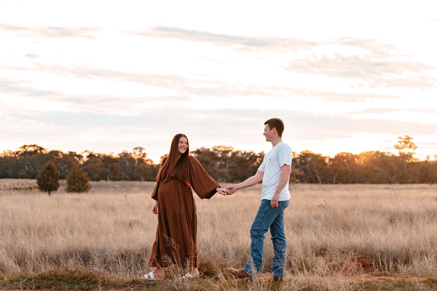 Pregnant mum expecting her 1st born. Outside at sunset & candidly walking, holding her partners hand as they look at each other lovingly