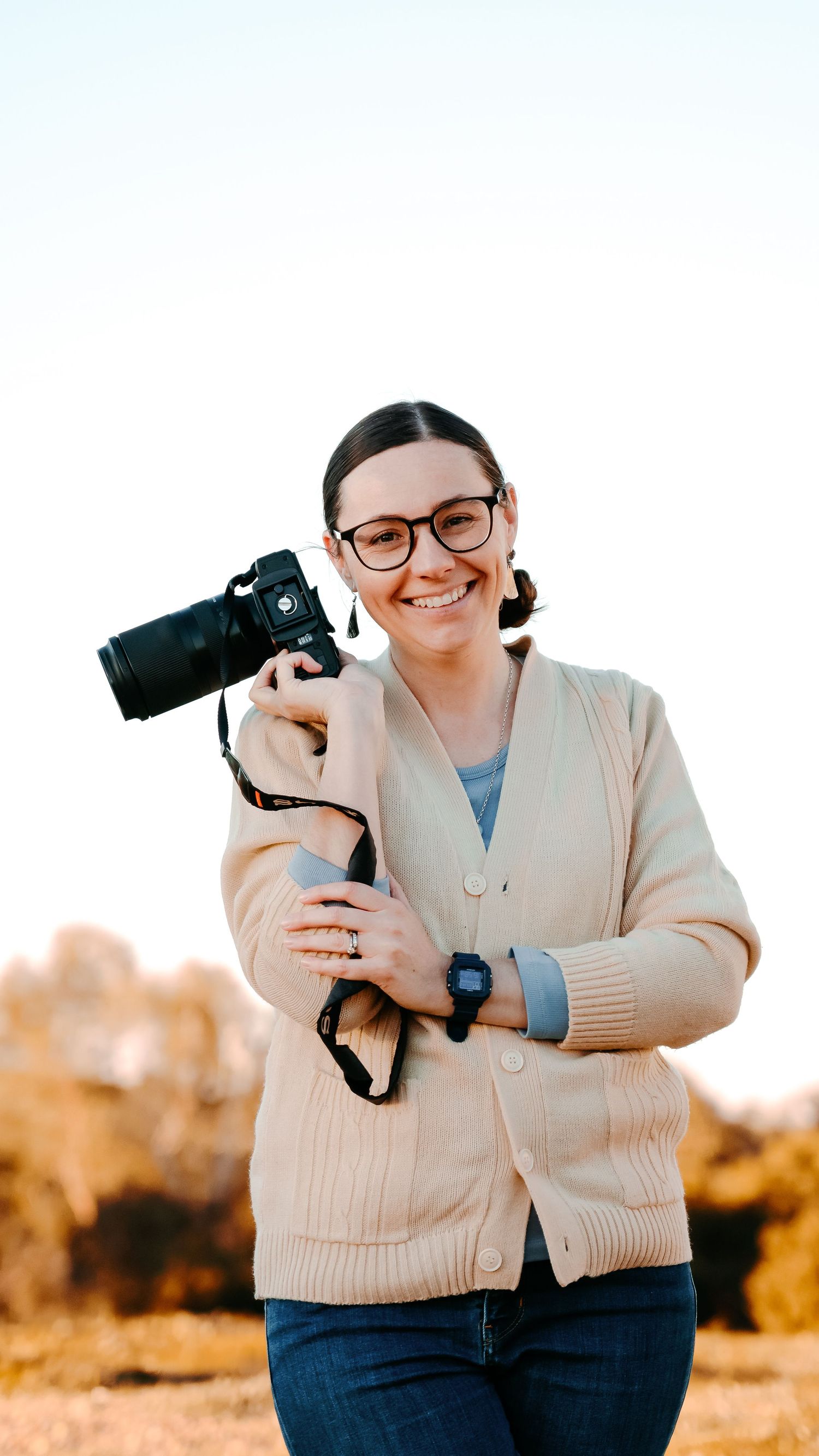 image of photographer holding a camera next to her hear. a clear shot of her smiling face to help people feel comfortable