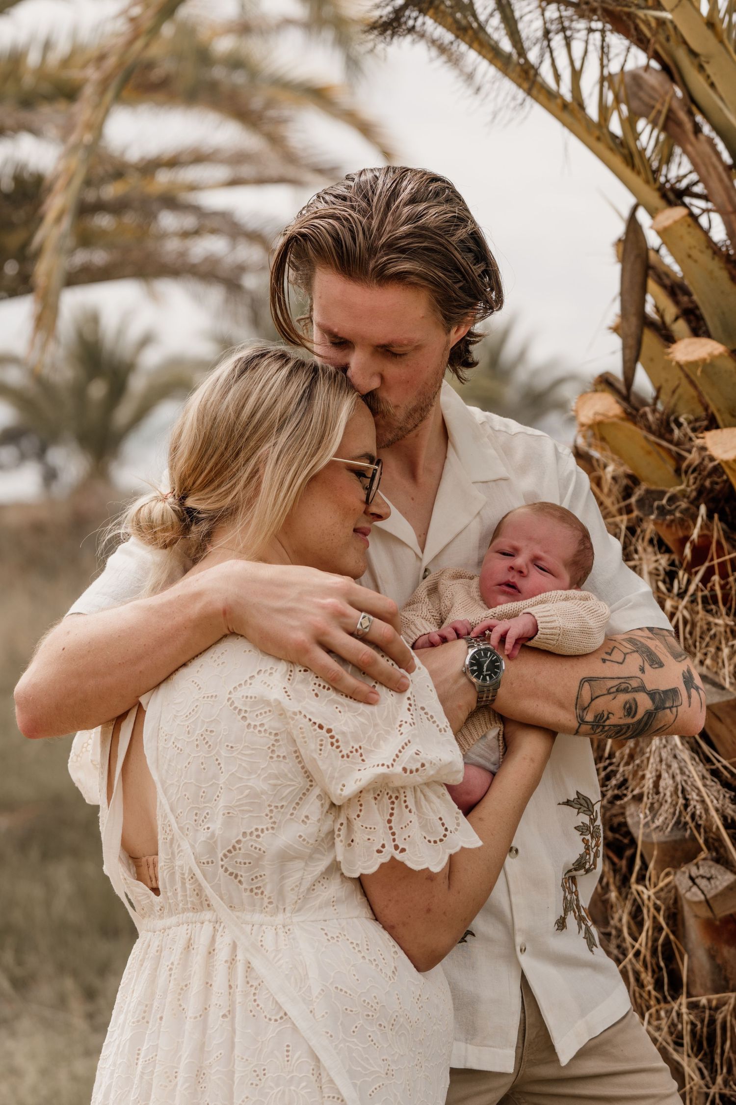 A proud father embracing his wife who has given birth to his new son. The father his kissing his wife on the head as they also hold the baby